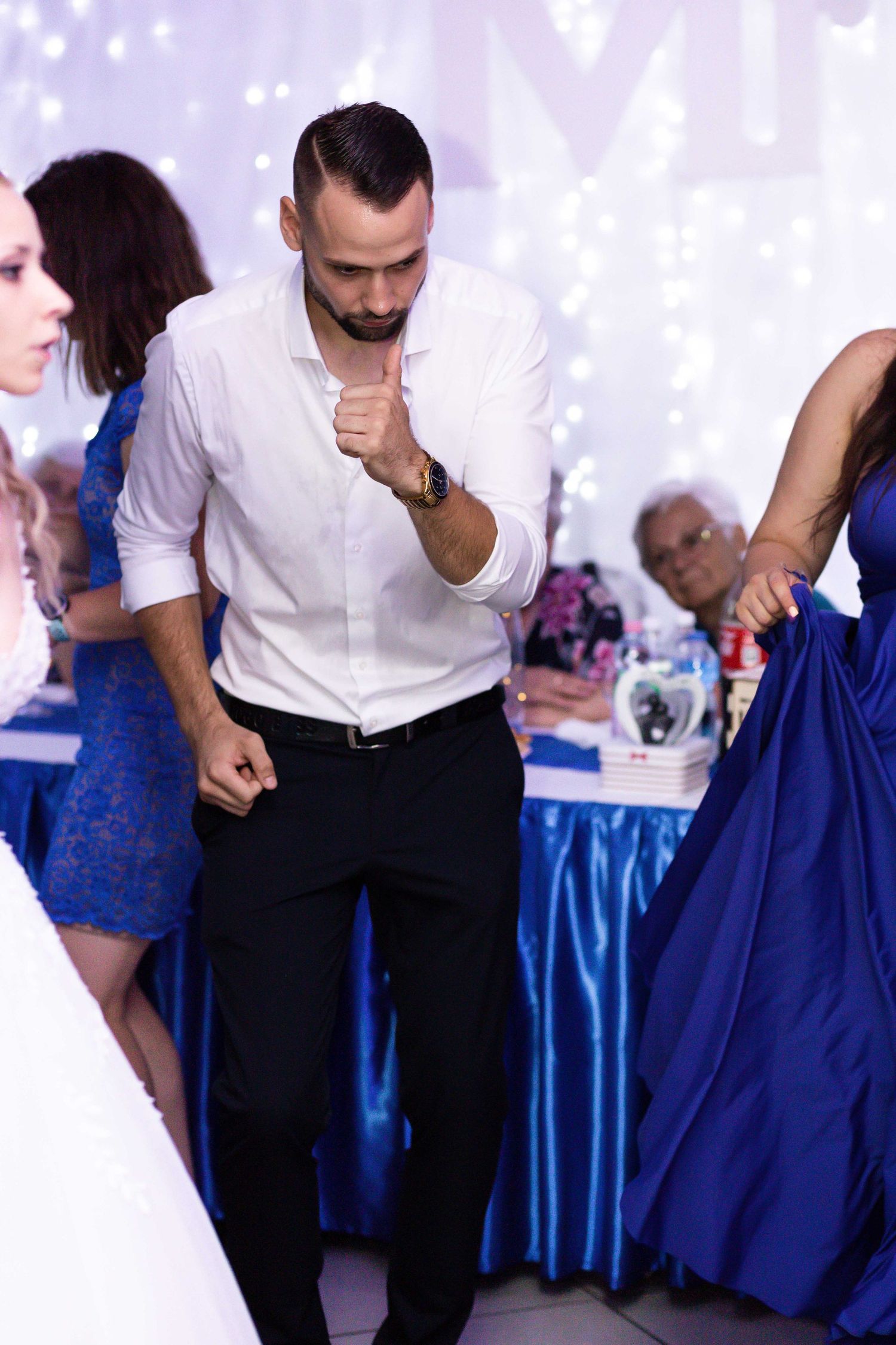 A couple in blue and white formal attire dancing together at an elegant event with sparkly decorations in the background.