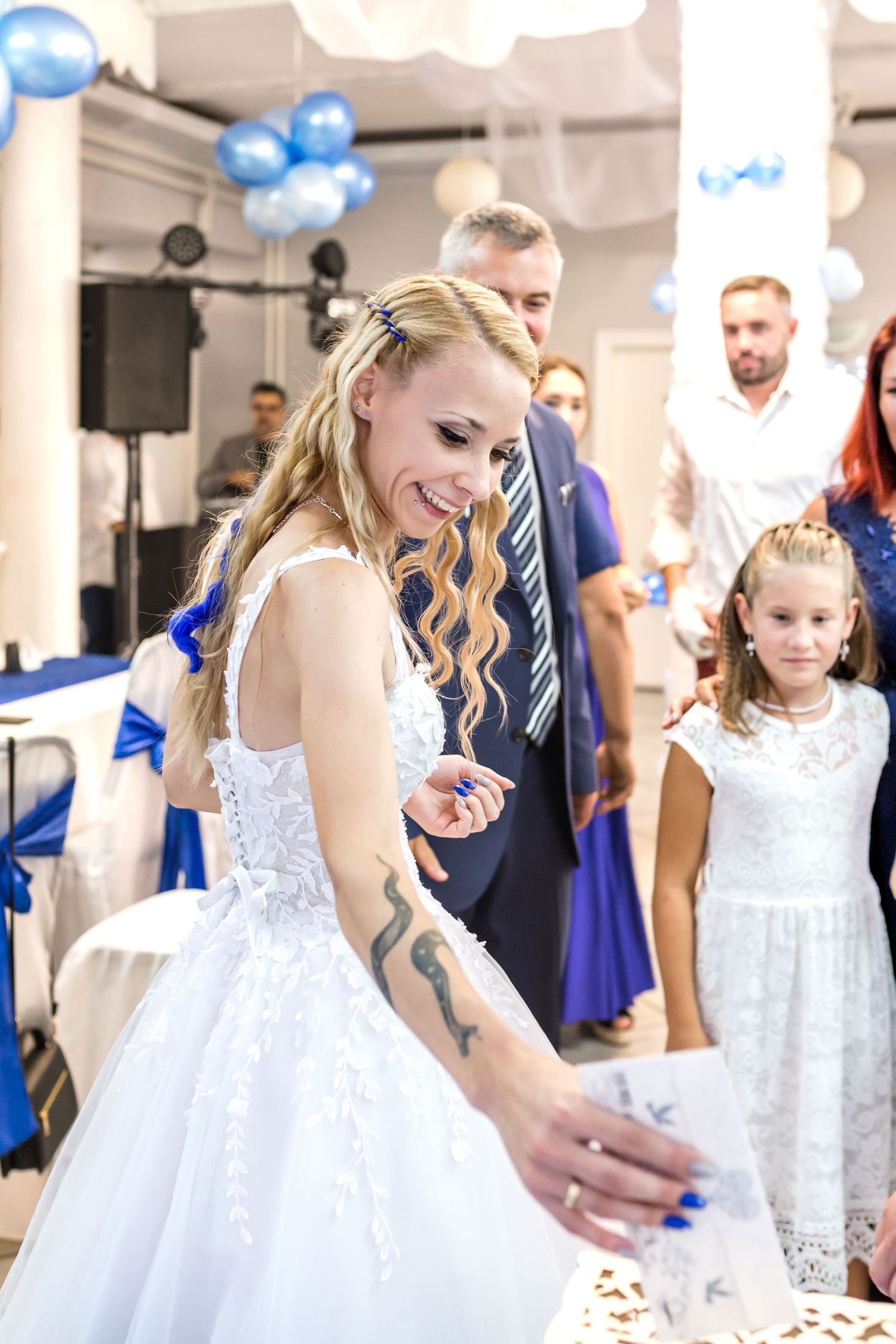 A bride in a white lace wedding dress celebrates at a reception decorated with blue balloons.