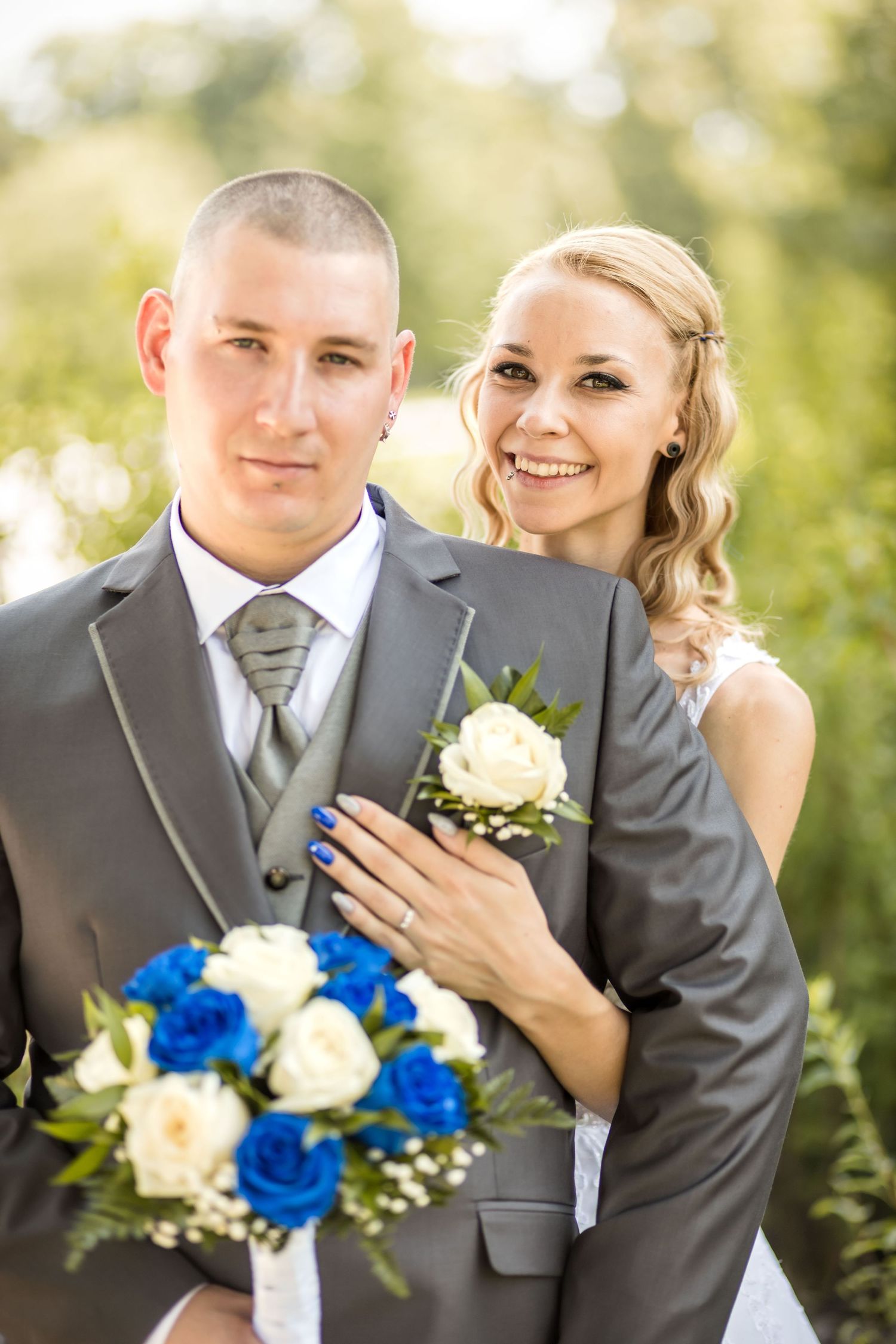 A bride and groom pose together outdoors with a bouquet of blue and white roses on their wedding day.
