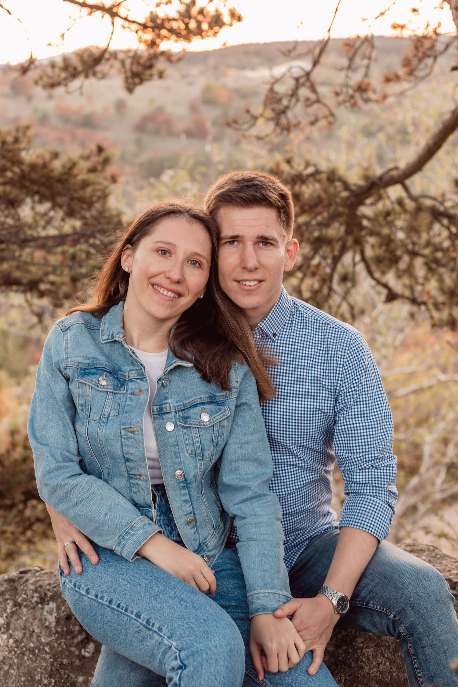 Romantic couple in matching denim outfits sitting together on rocks during golden hour.