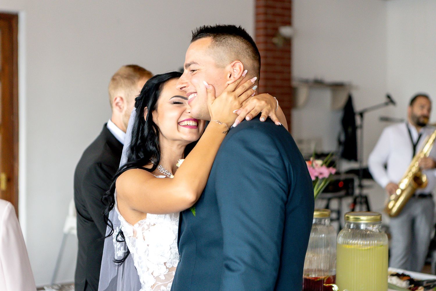 A couple shares a joyful moment during their wedding reception as guests celebrate in the background.