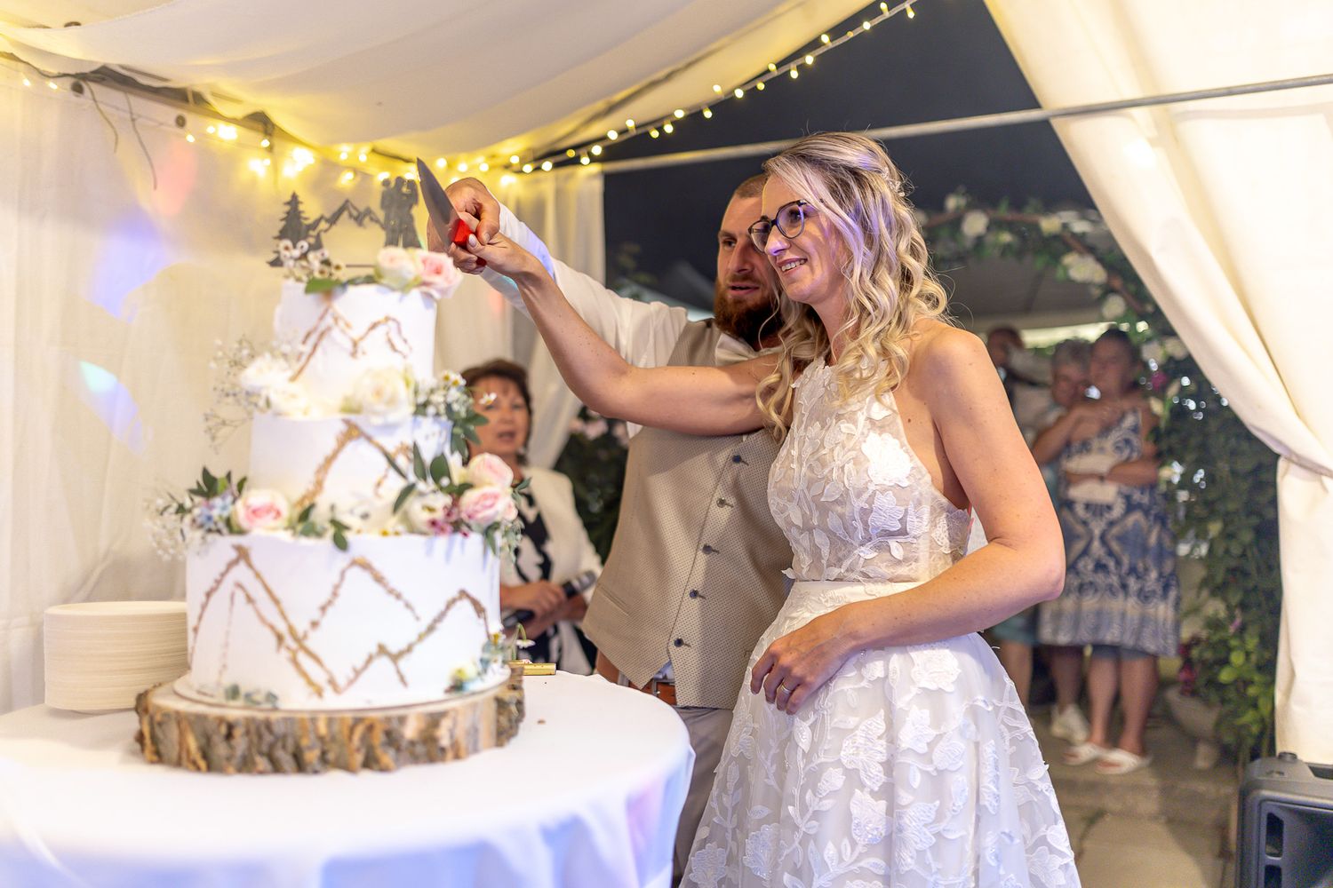 A bride and groom share their first dance under a white tent decorated with twinkling lights at their wedding reception.