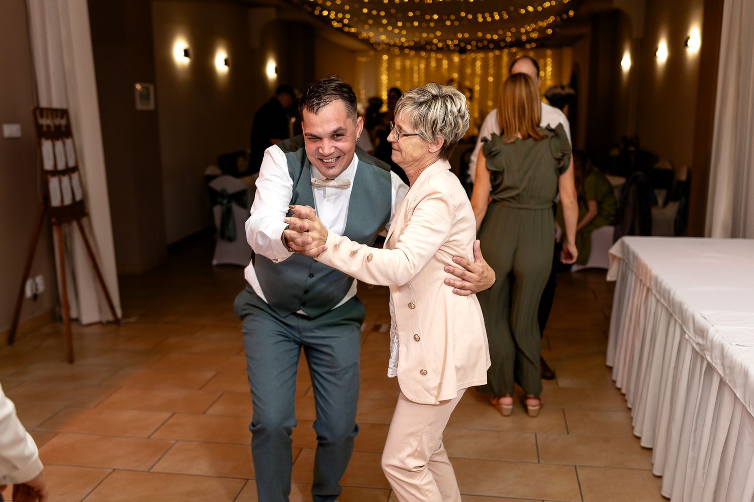 A couple dances together under twinkling string lights during a wedding reception celebration.