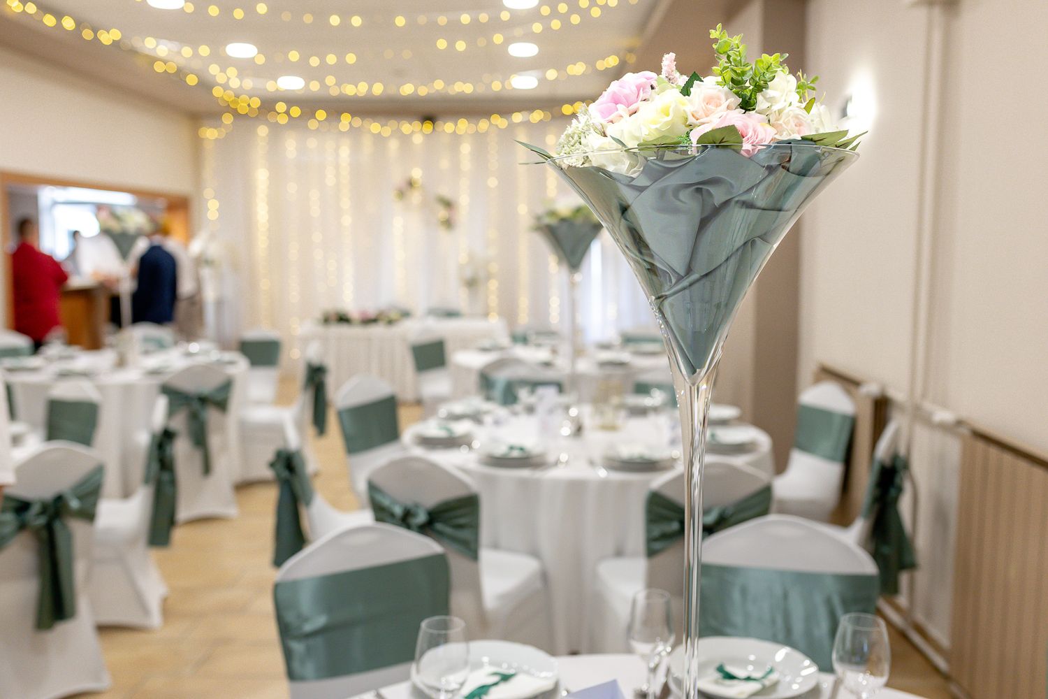 Elegant wedding reception venue with white drapes, string lights, and teal accents on dining tables.