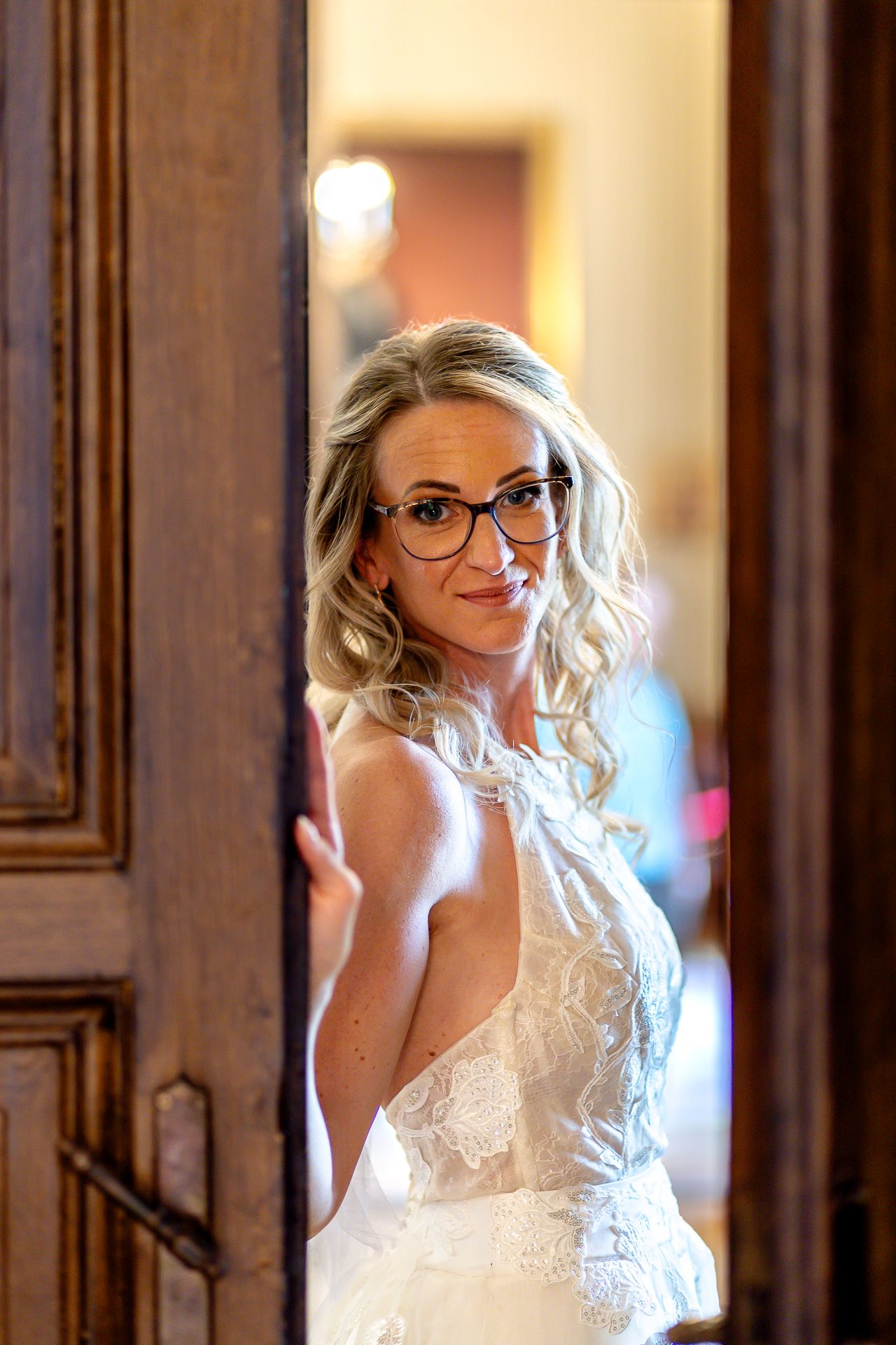 A bride in a white wedding dress and glasses poses elegantly in a series of photos with warm lighting and wood paneling.