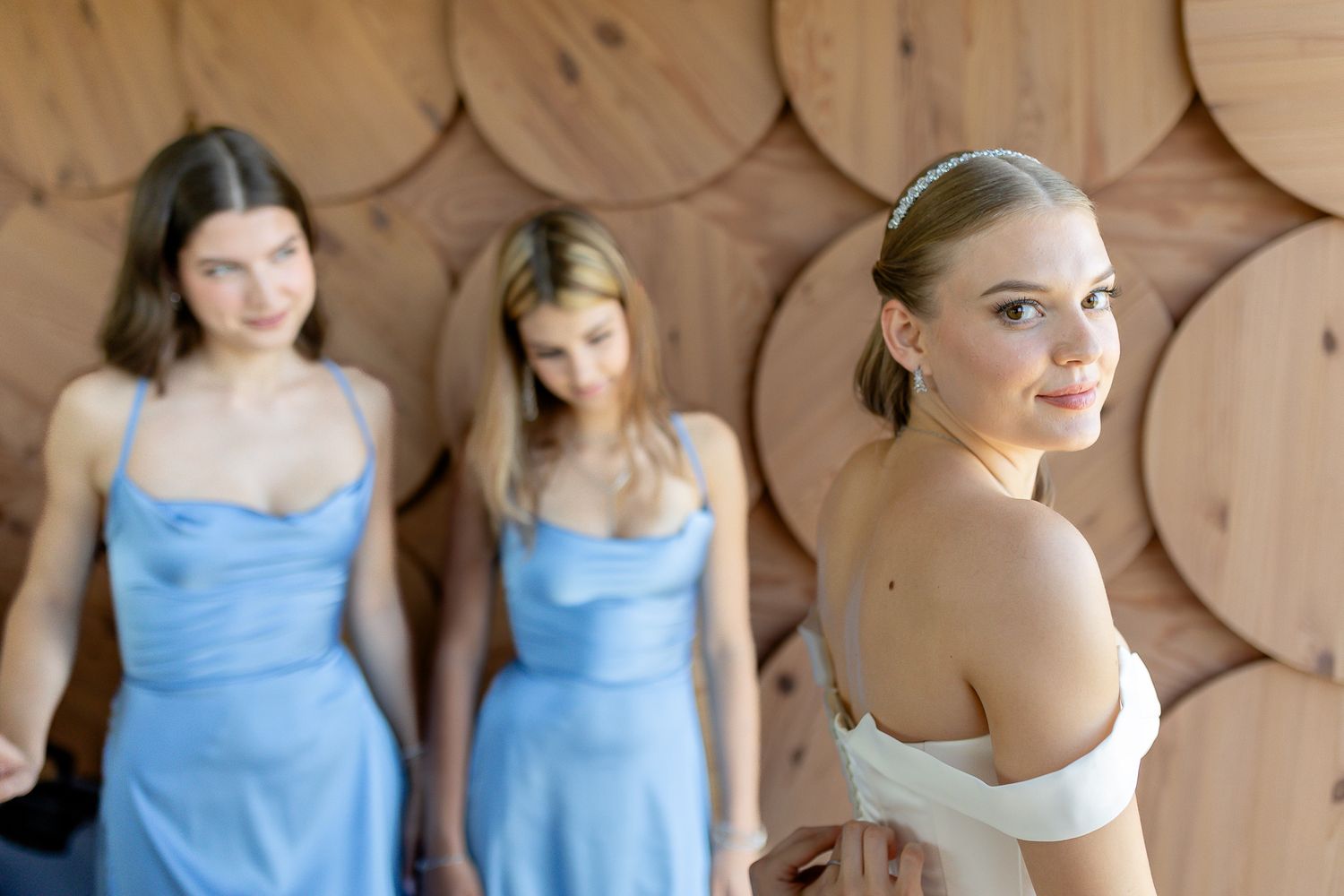A bridal party poses against wooden wall decor with bridesmaids in blue dresses.