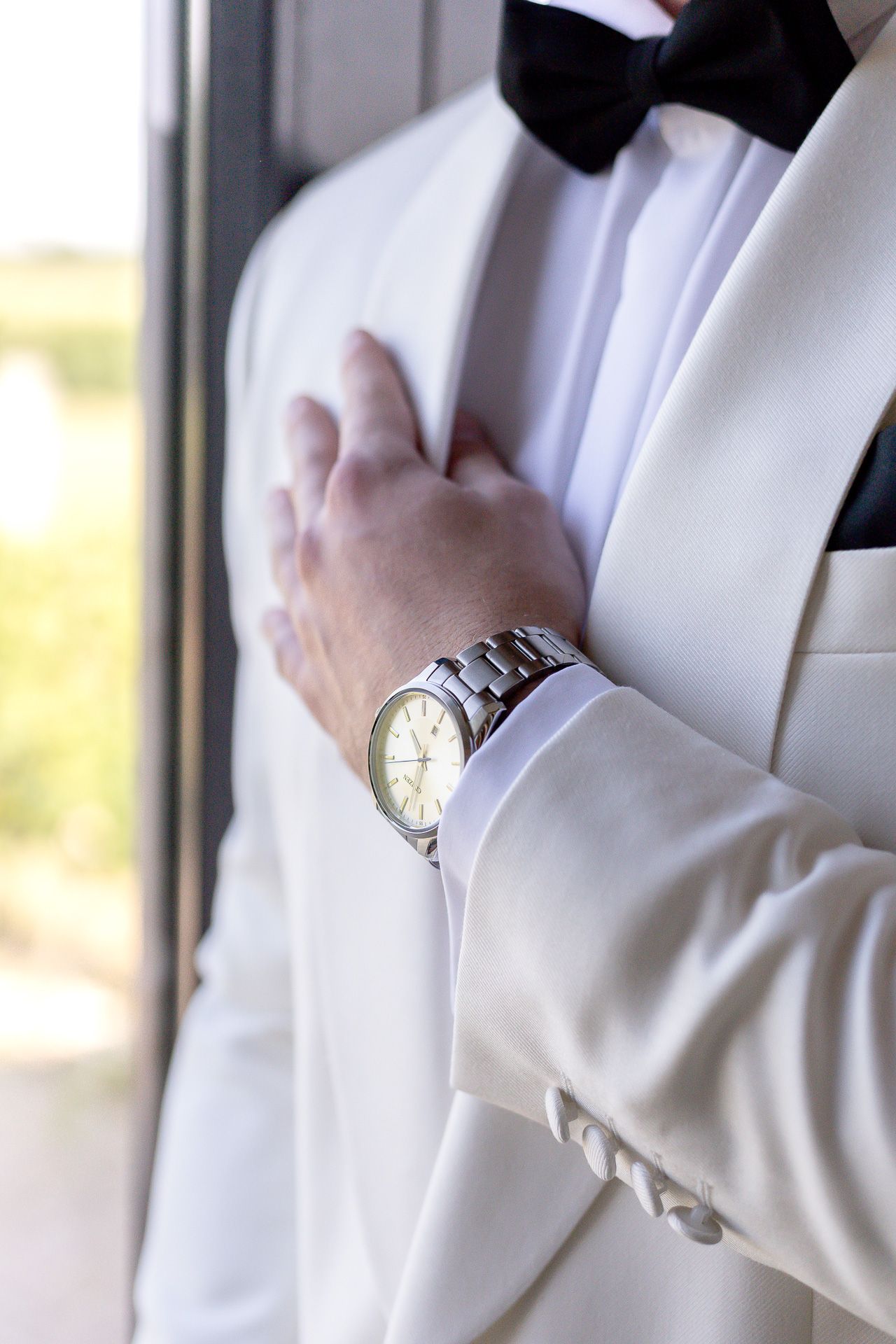 Close-up of a silver wristwatch worn with a crisp white tuxedo sleeve.