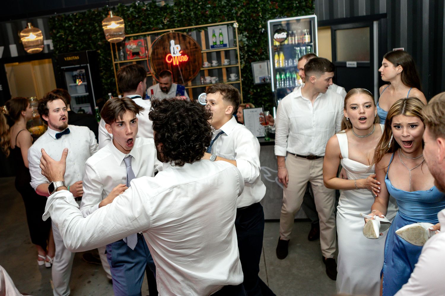 Lively wedding reception with guests dancing and celebrating in a venue with greenery decor.