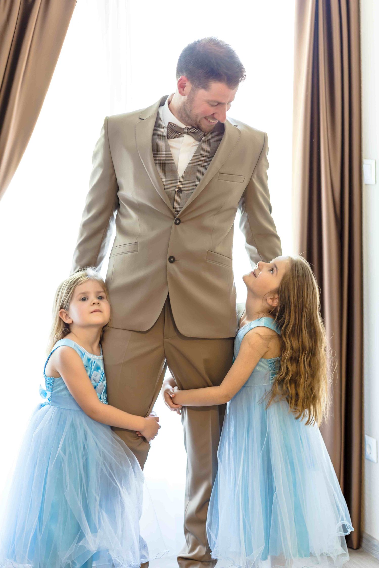 A parent in a tan suit dances with a young child wearing a light blue tulle dress in a series of candid moments.