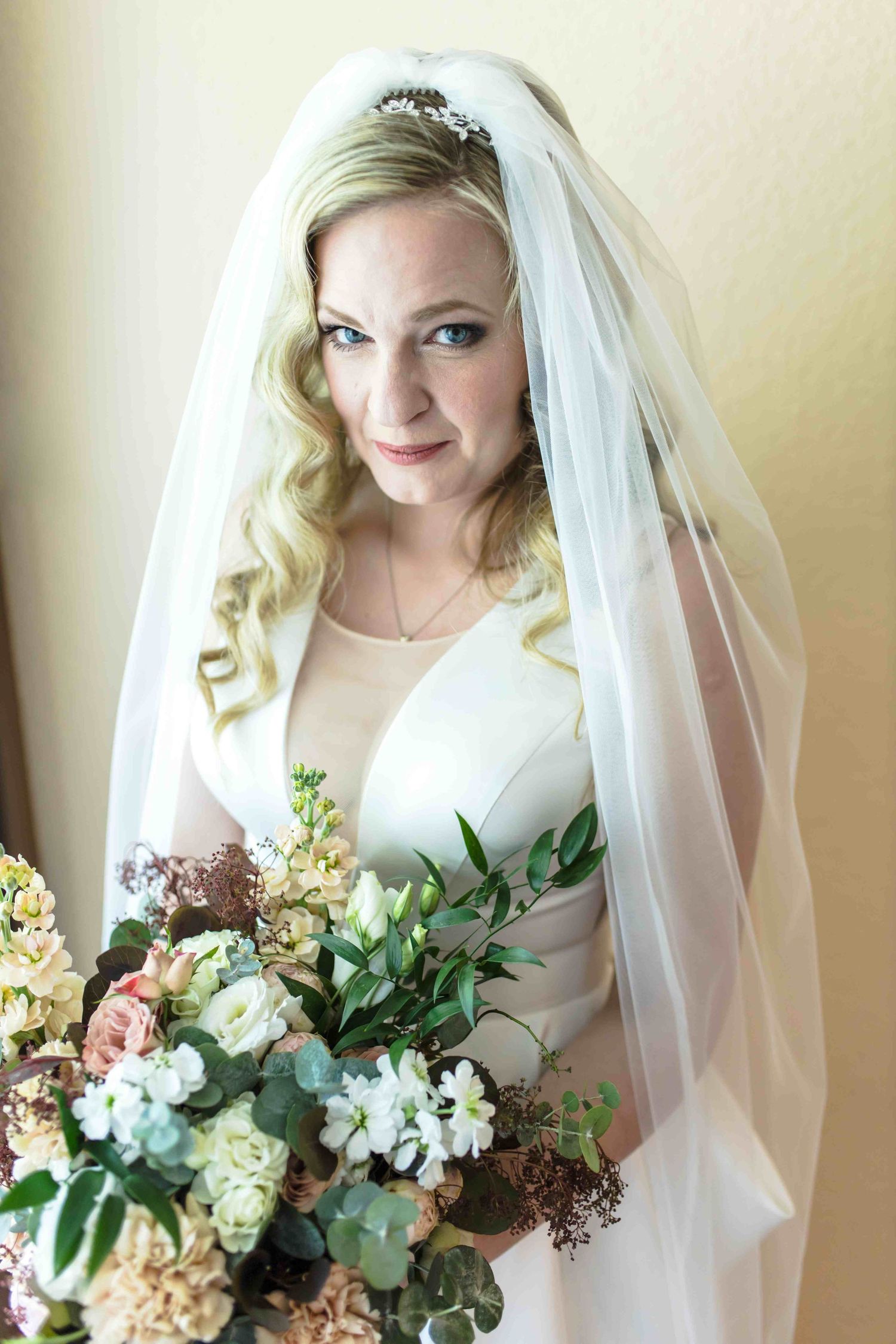 A bride in a white wedding dress holds a romantic bouquet of peach and white flowers with greenery.