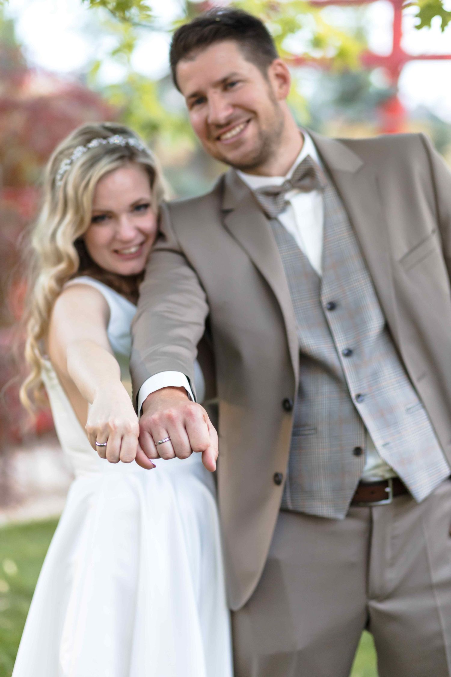 A bride and groom in gray suits share joyful moments together during an outdoor wedding photoshoot.