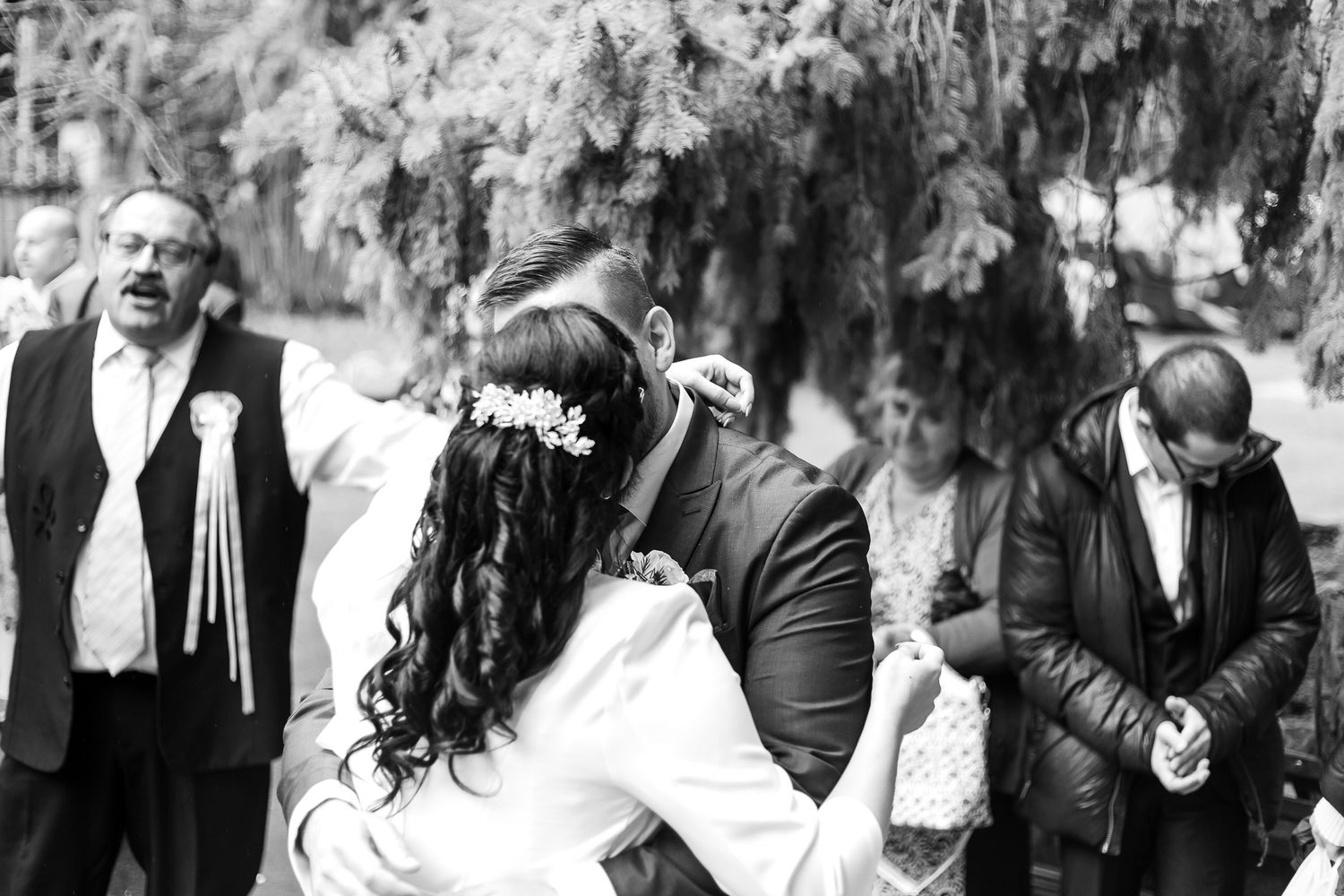 A black and white candid moment captured during an outdoor wedding ceremony under hanging trees.