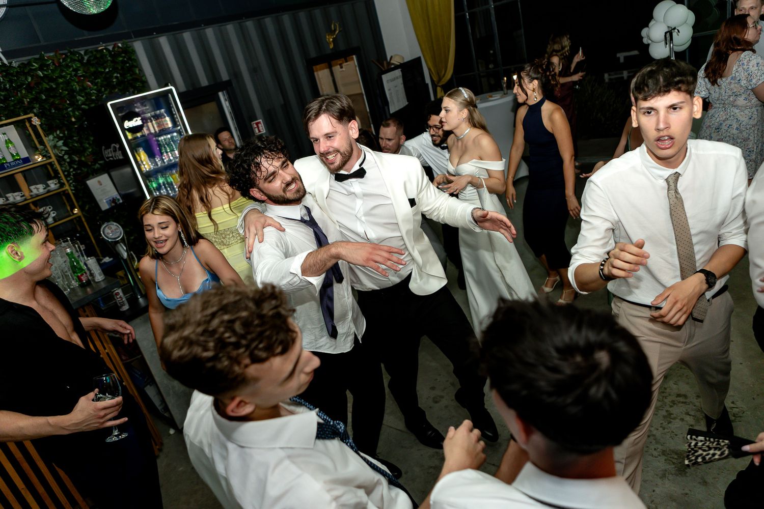 Guests dancing and socializing at a dimly lit indoor wedding reception.