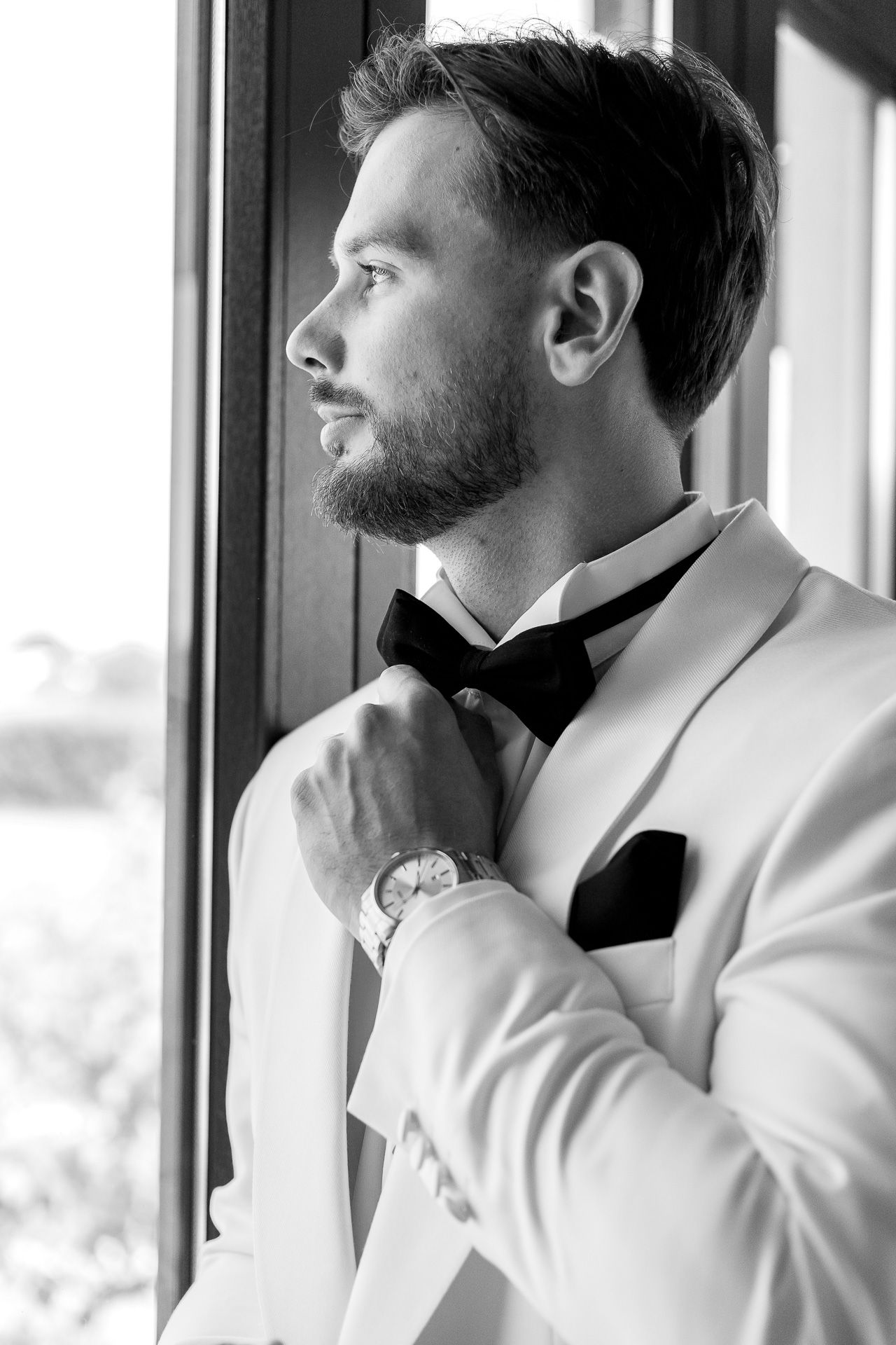 Side profile view of someone in a white tuxedo and black bow tie looking out a window.