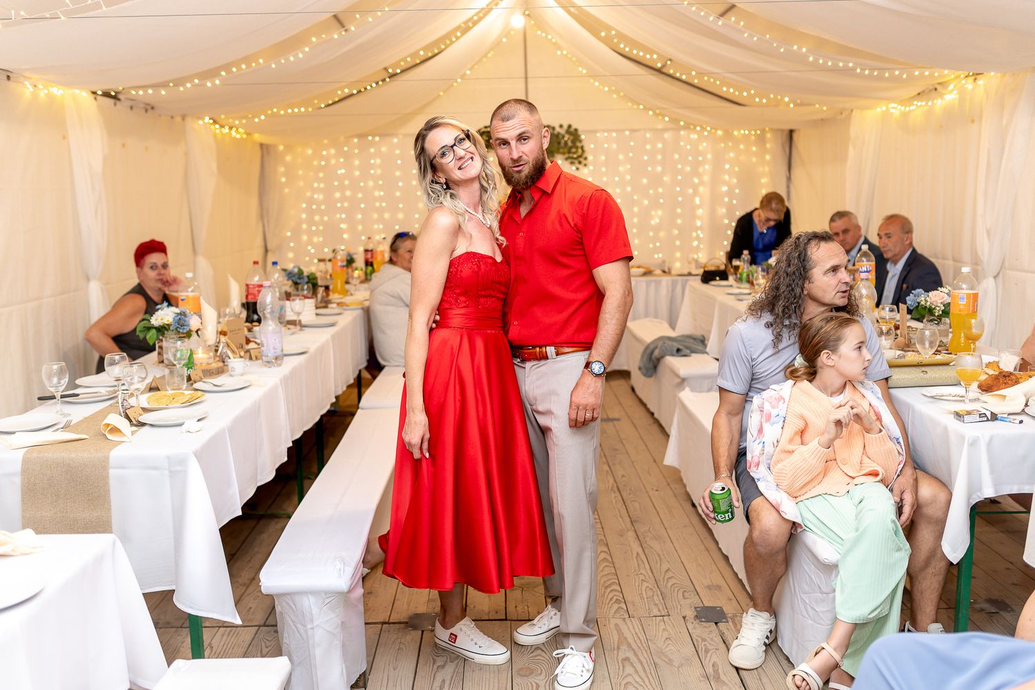 Wedding reception setup in an elegant white tent with round tables and red accent decorations.