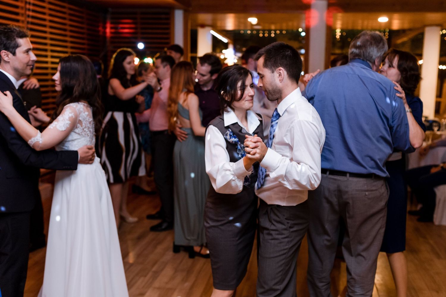 Wedding guests dancing in a dimly lit barn venue with wooden walls and romantic lighting.
