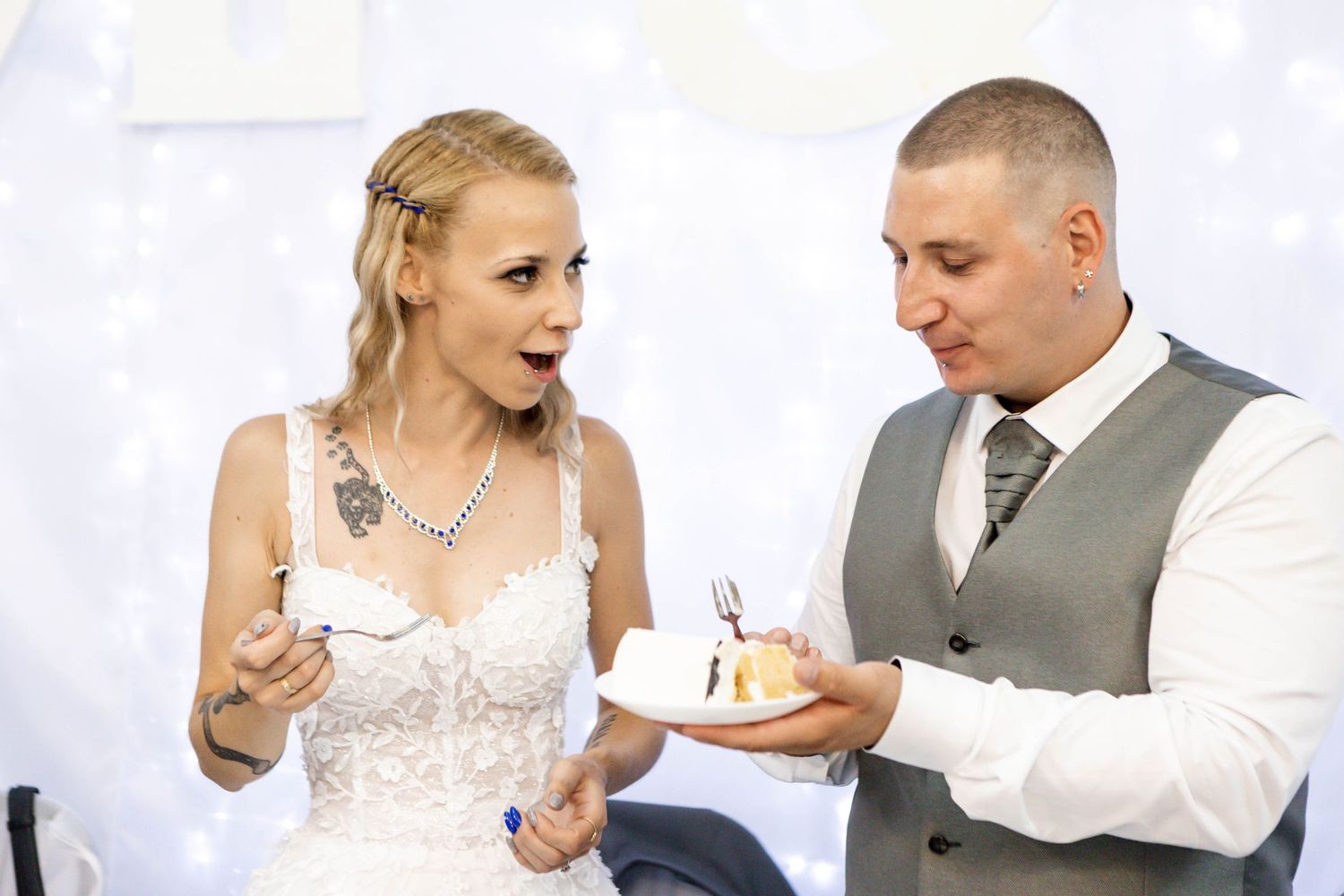 A couple in wedding attire shares a piece of cake during their reception celebration.