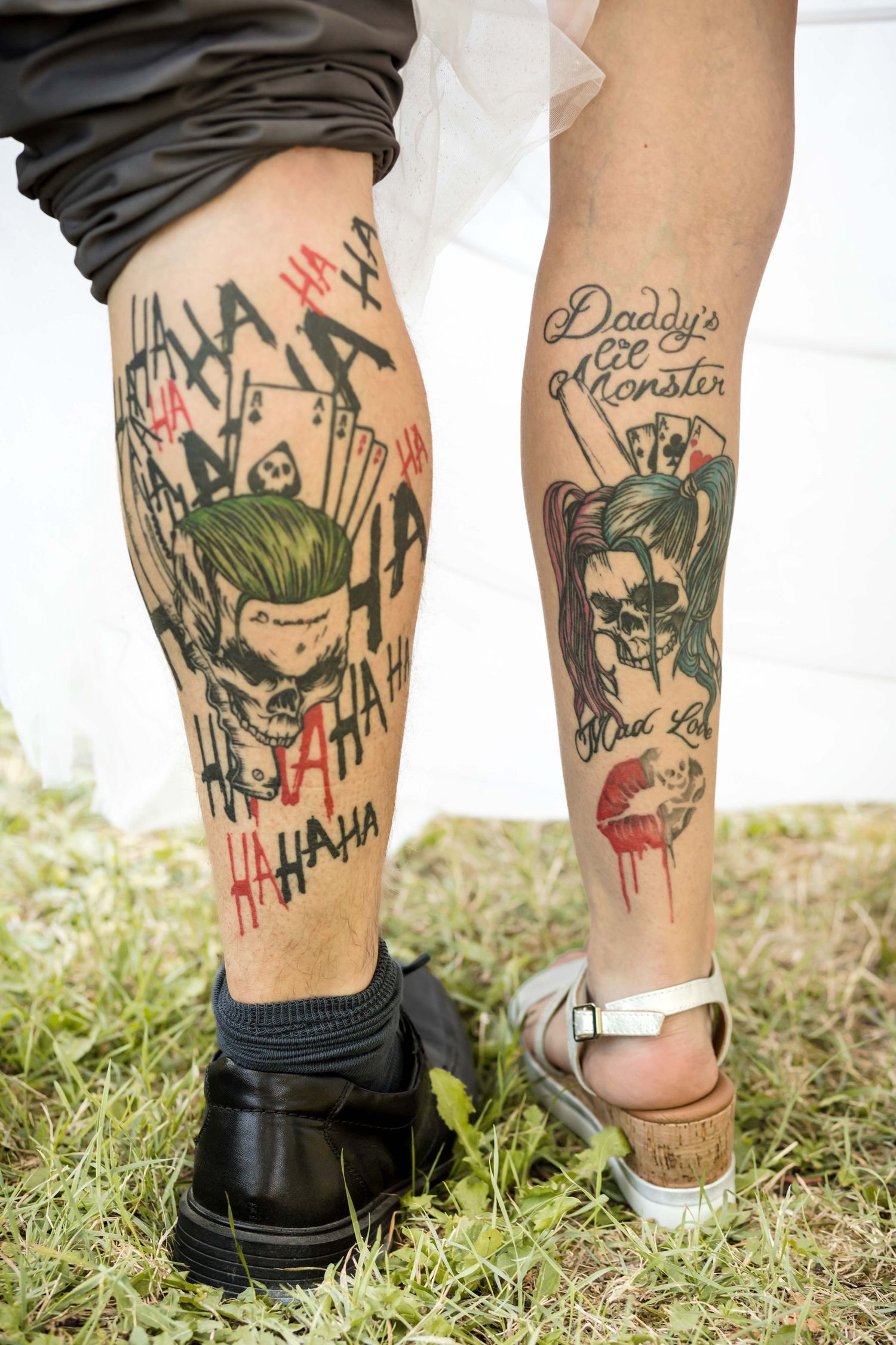 A series of colorful tattoos featuring comic-style art and text designs displayed on someone's legs in grass.