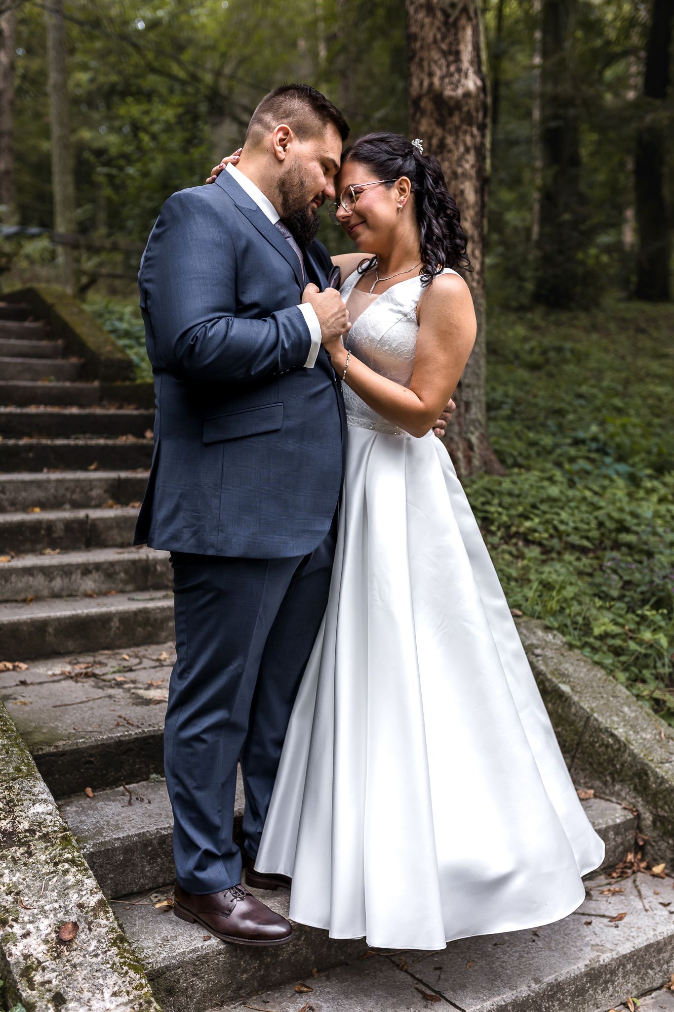 A romantic moment between newlyweds on stone steps surrounded by lush greenery in an outdoor garden setting.