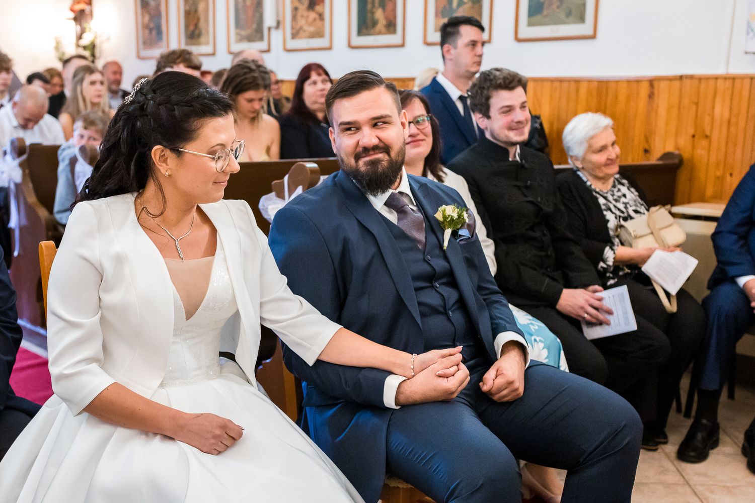Wedding guests laugh and smile during a reception in a wood-paneled venue with framed portraits on the wall.