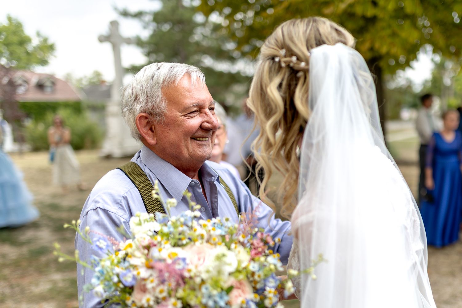 A joyful moment shared between someone and a bride holding a colorful wildflower bouquet at an outdoor wedding ceremony.