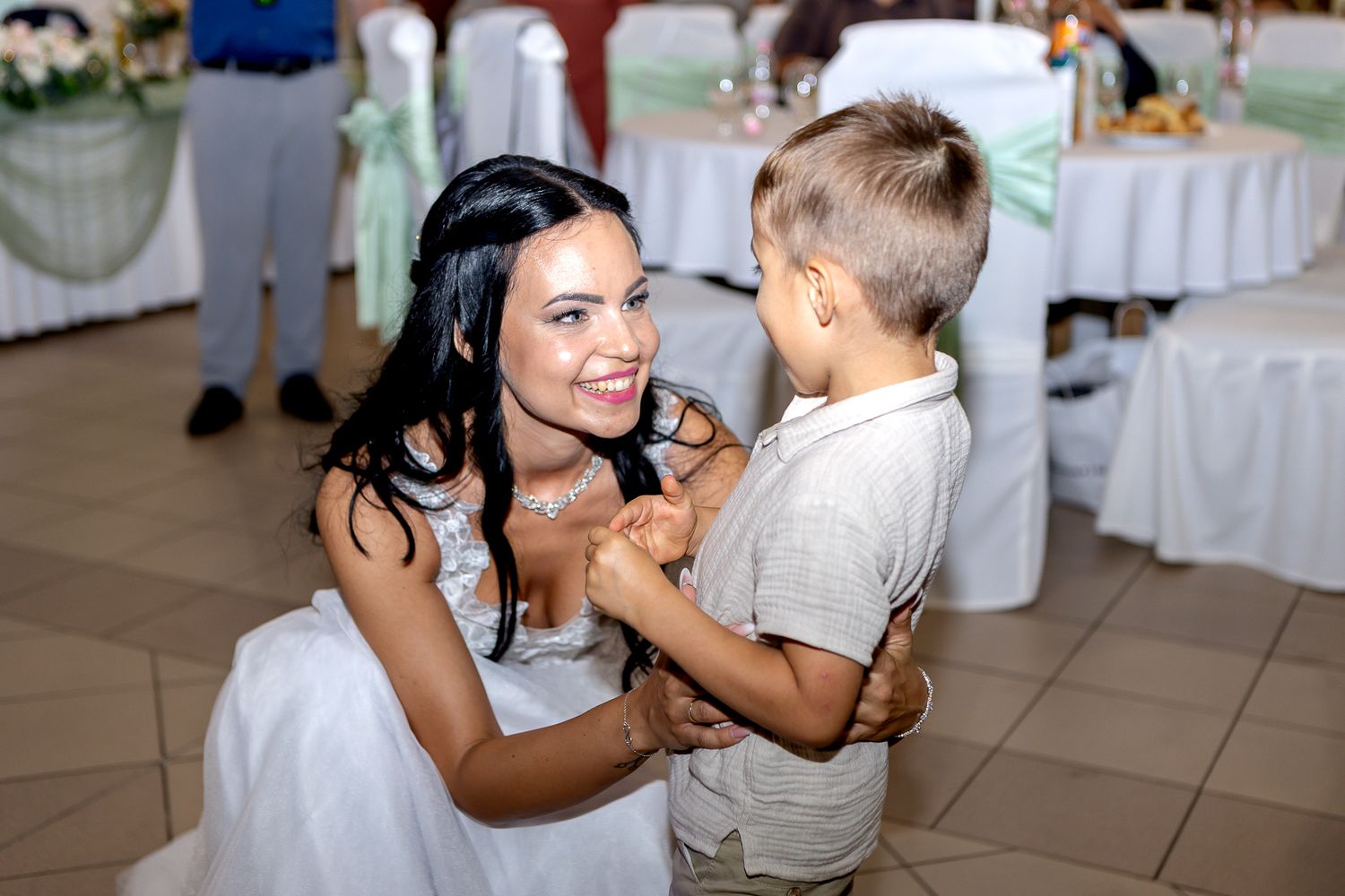 A couple shares a tender dance together at a wedding reception on a white tiled floor.