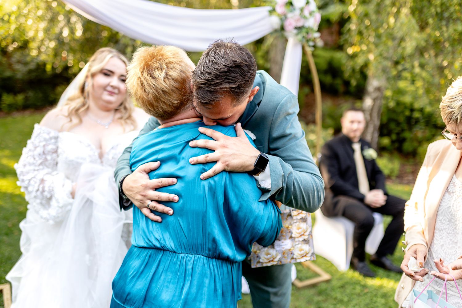 A heartfelt embrace is shared between two people wearing blue and black at an outdoor gathering.