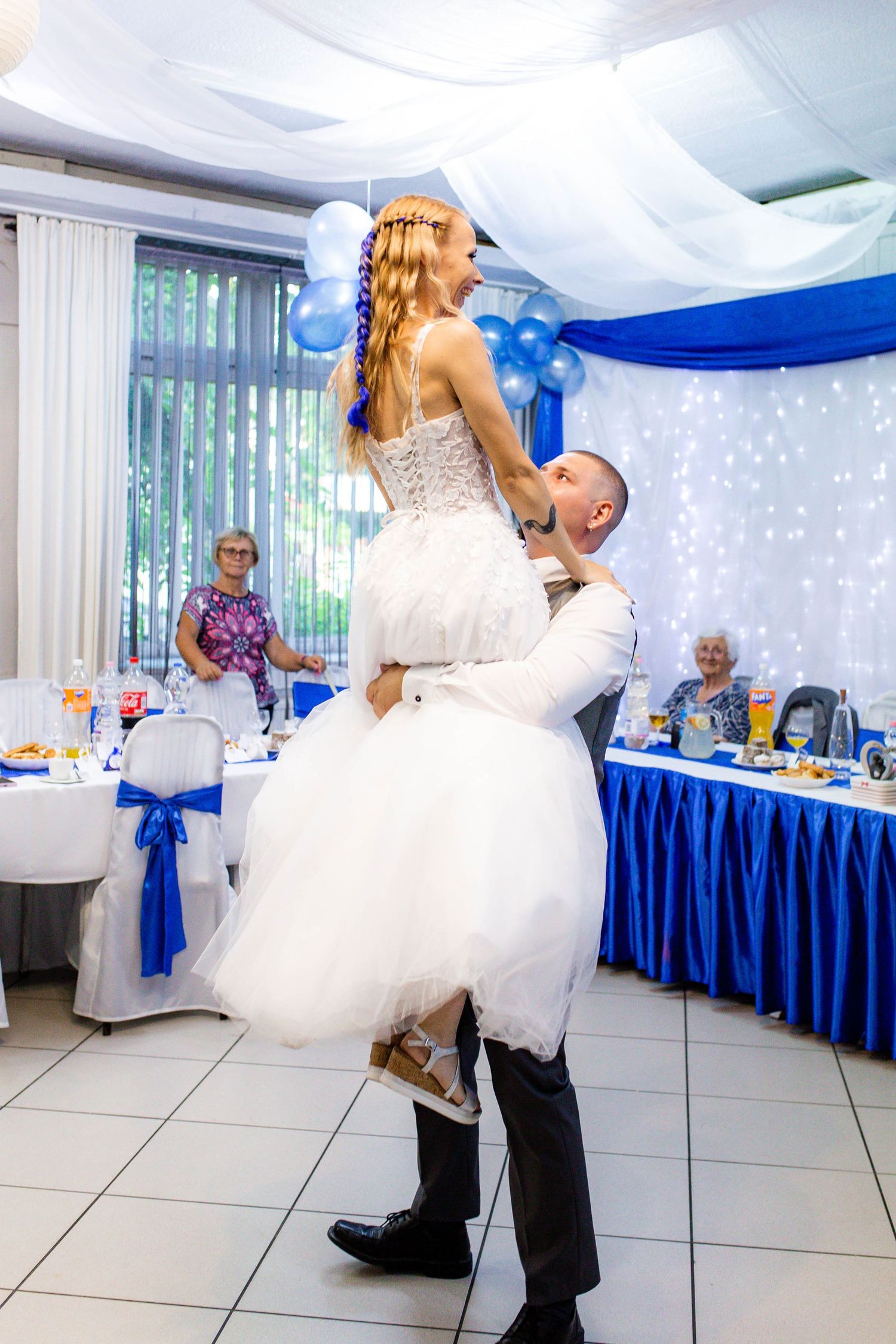 Newlyweds share their first dance in a reception hall decorated with royal blue and white accents.