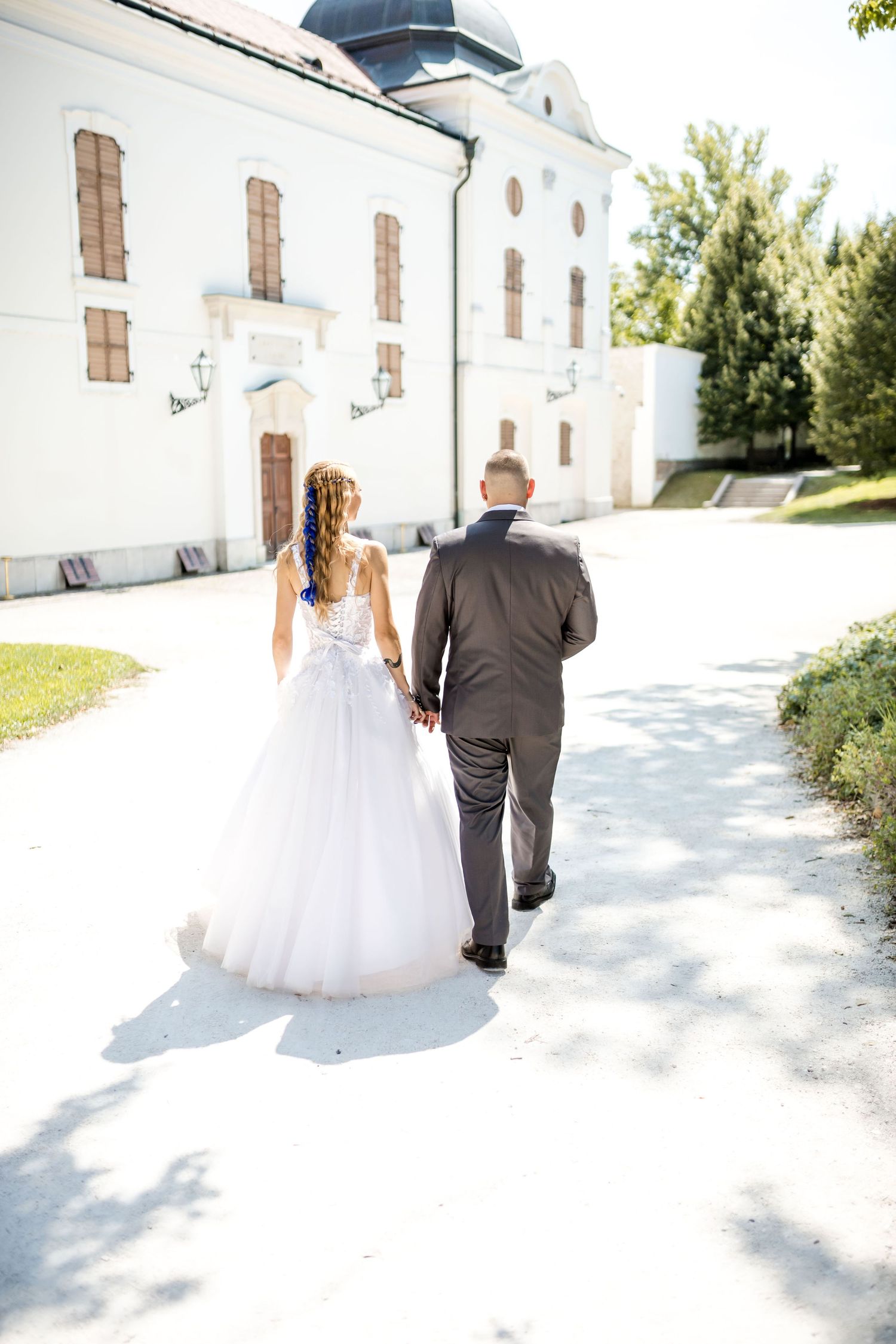 A couple in wedding attire walks along a white pathway next to a church building on their special day.