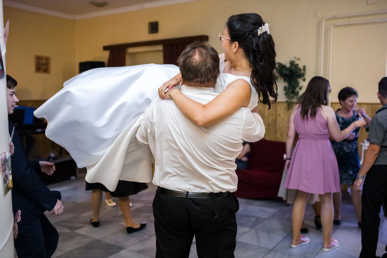 Wedding couple dances together while guests enjoy the celebration in a reception hall.