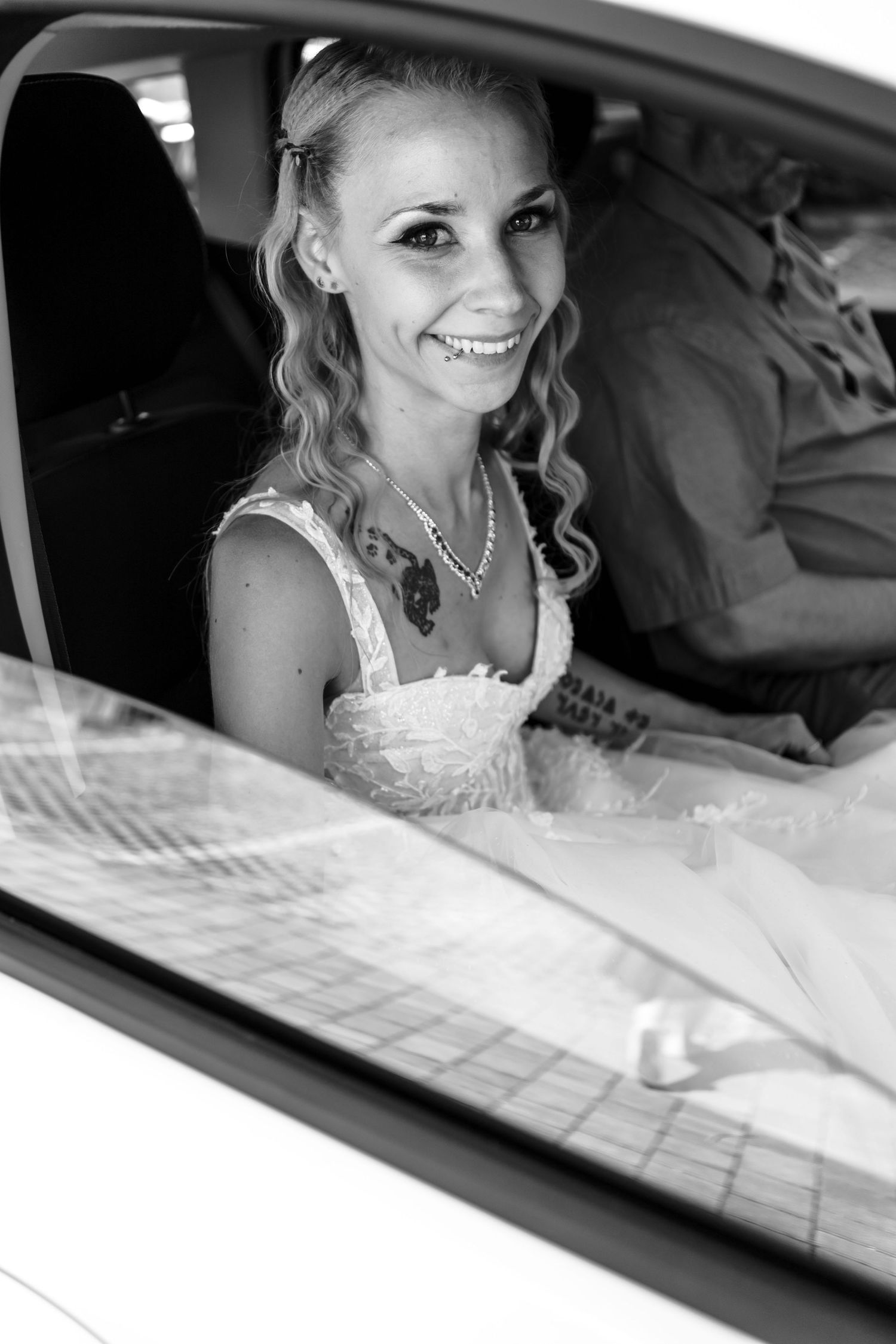 A bride in a white dress sits in a car smiling through the window in a series of black and white photographs.