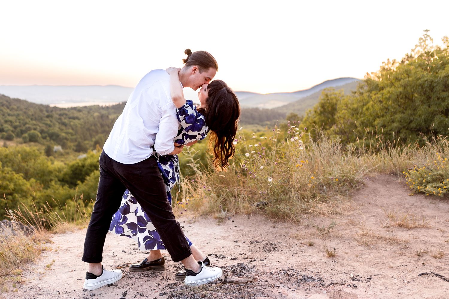A couple plays around on a mountain trail during a sunset photoshoot.
