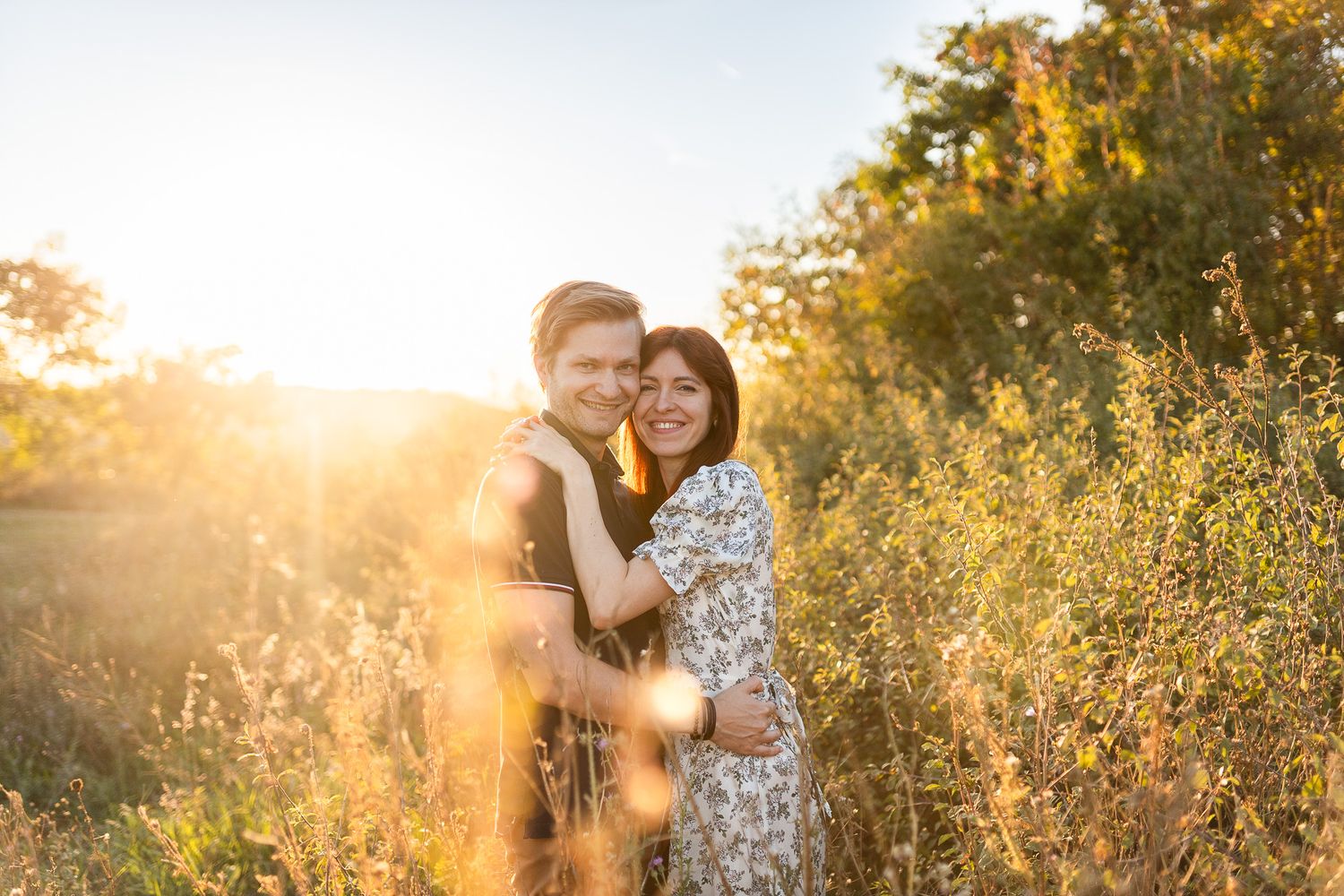 Couple poses together at sunset in a golden field with glowing sunlight creating a romantic atmosphere.