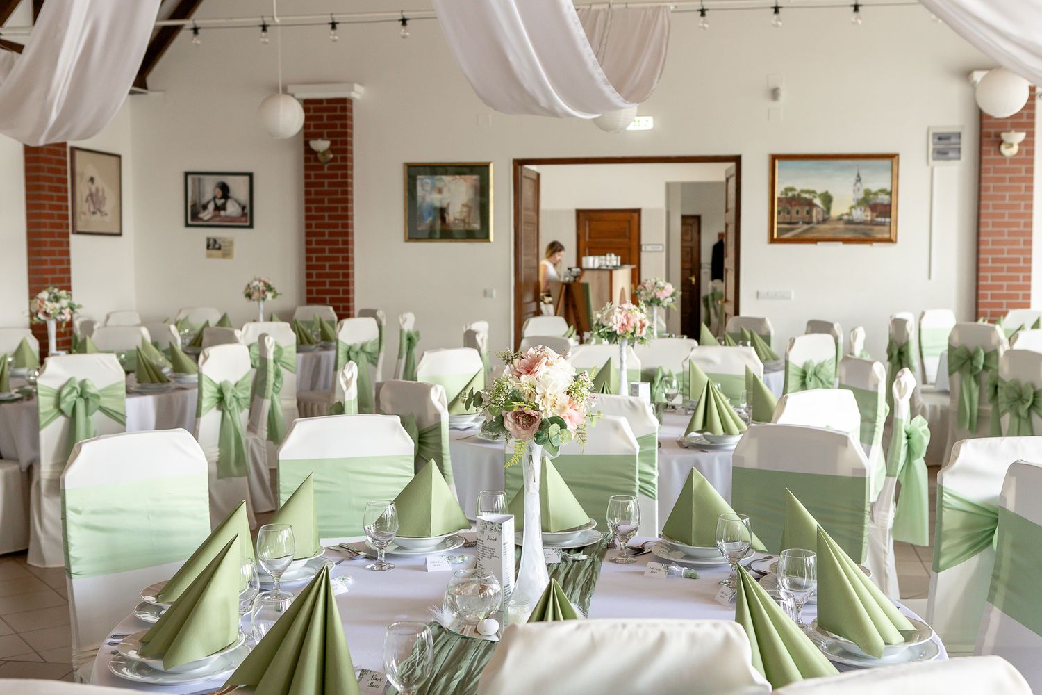 Wedding reception venue decorated with elegant white and mint green table settings and string lights overhead.