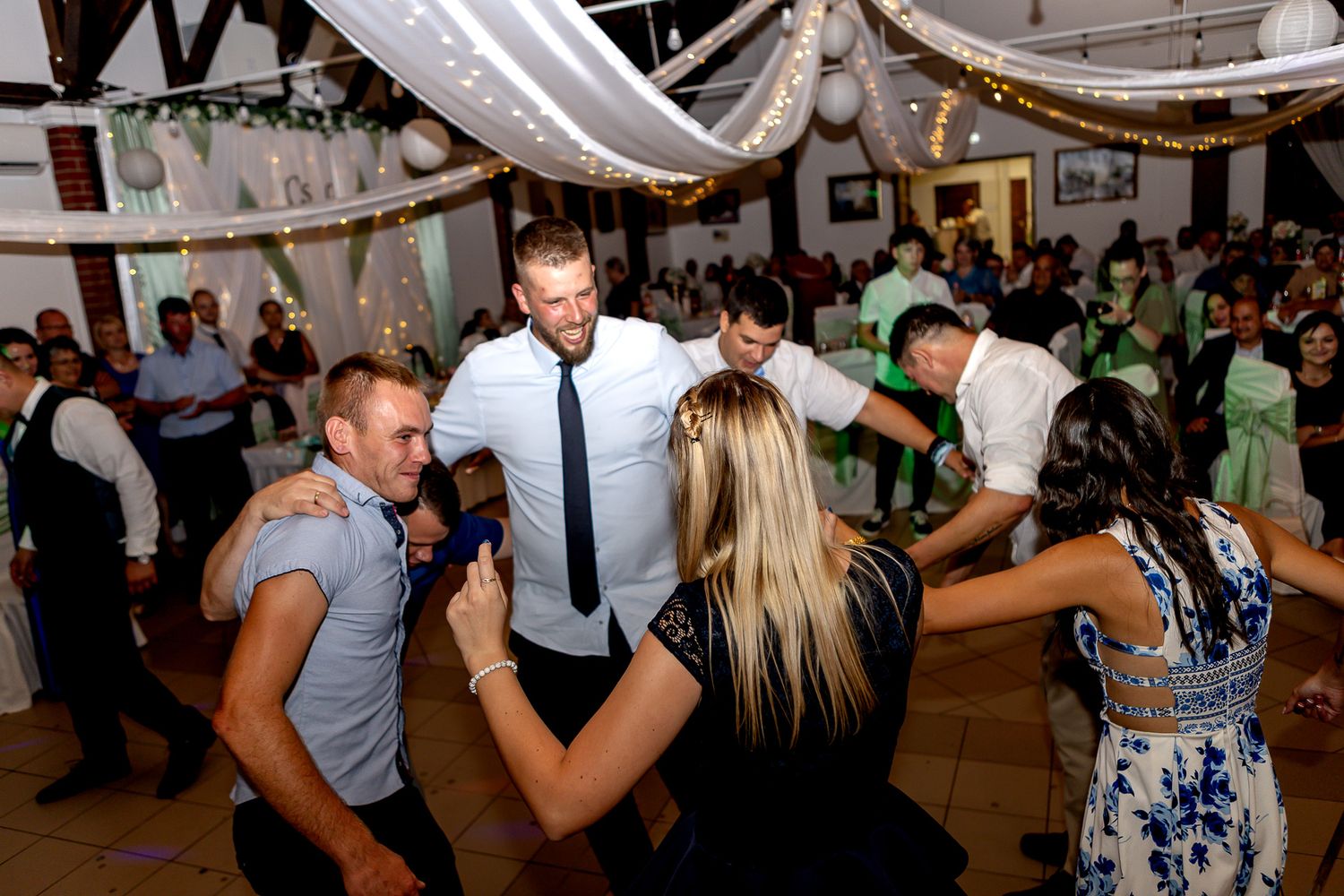 Couples dancing together at a lively indoor wedding reception with white fabric draped from the ceiling.