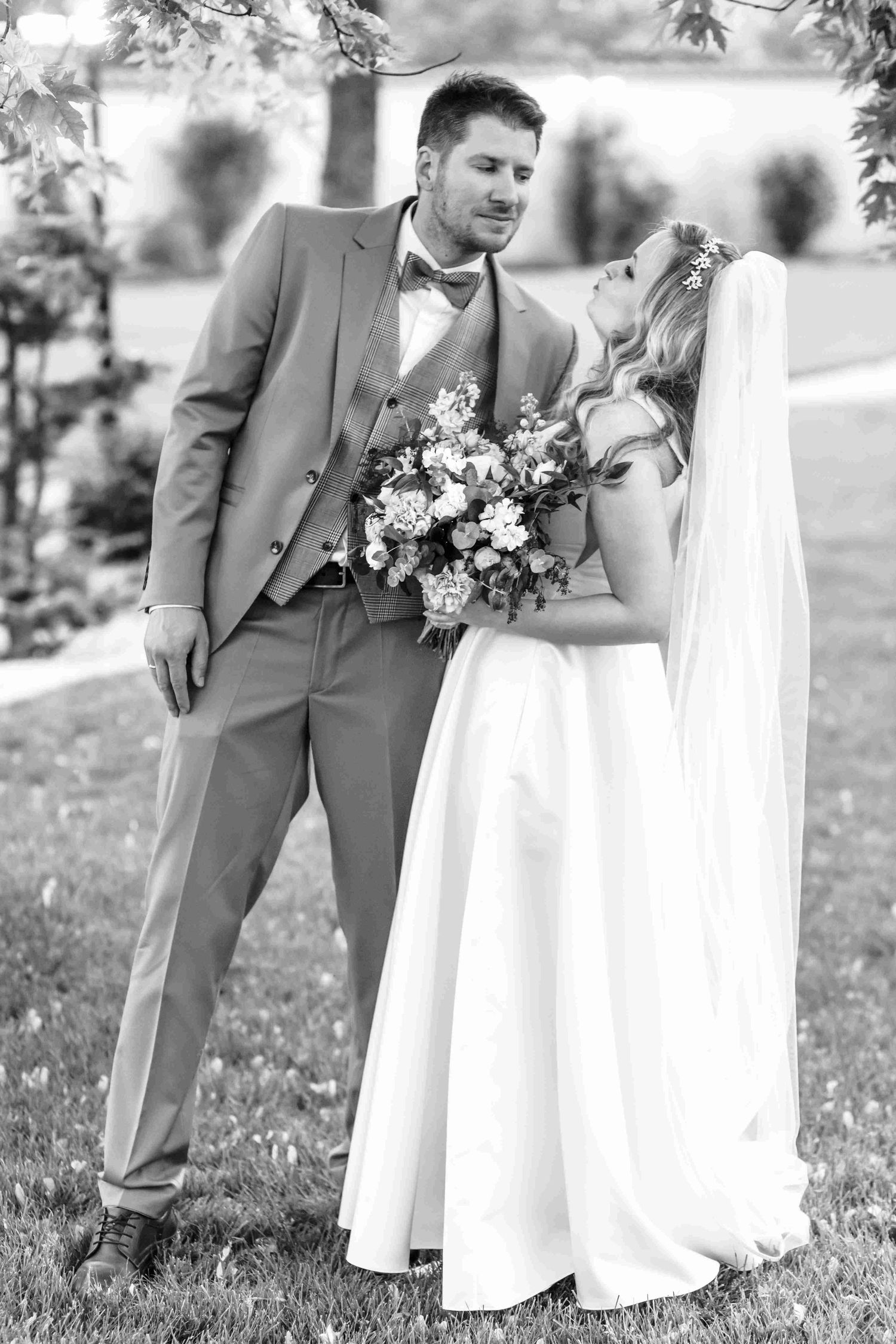 A black and white wedding photo showing a couple outdoors, with the bride holding a floral bouquet.
