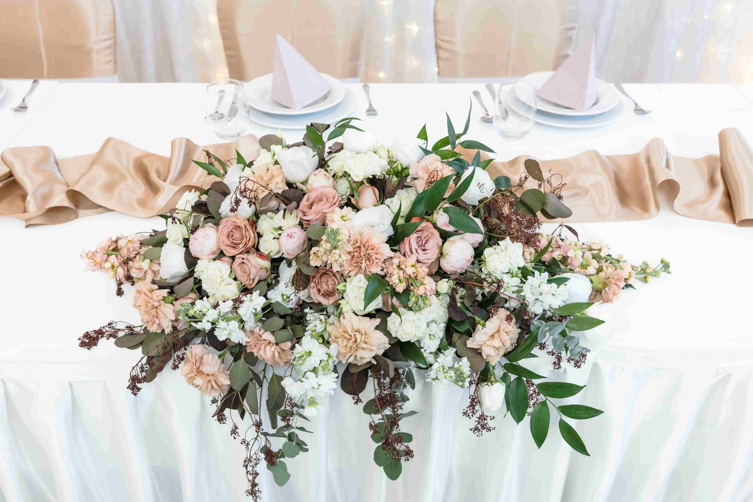 Long banquet table decorated with romantic floral arrangements and white table settings for a wedding.
