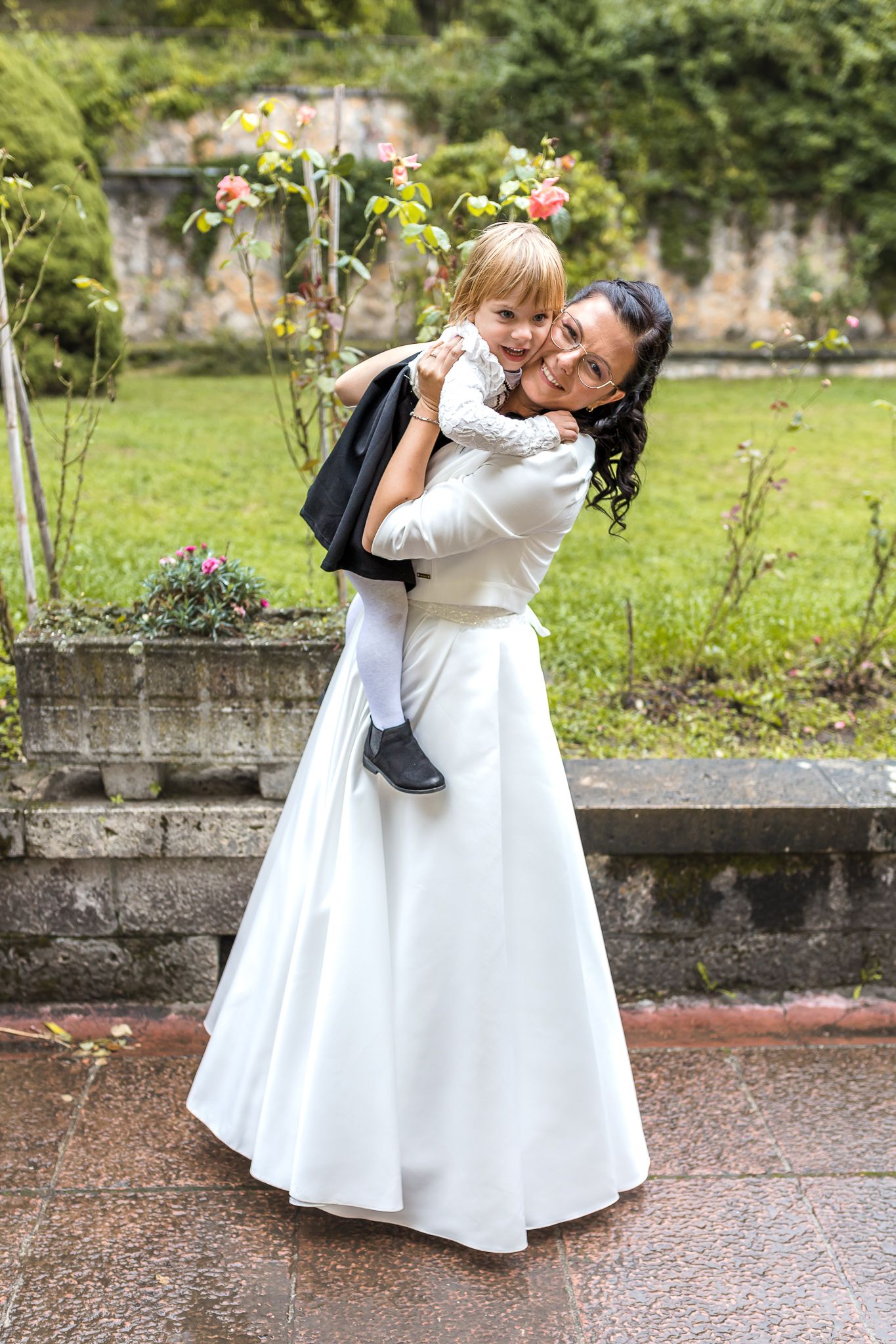 A heartwarming wedding moment captured in a garden setting as two people embrace and twirl in white dresses.