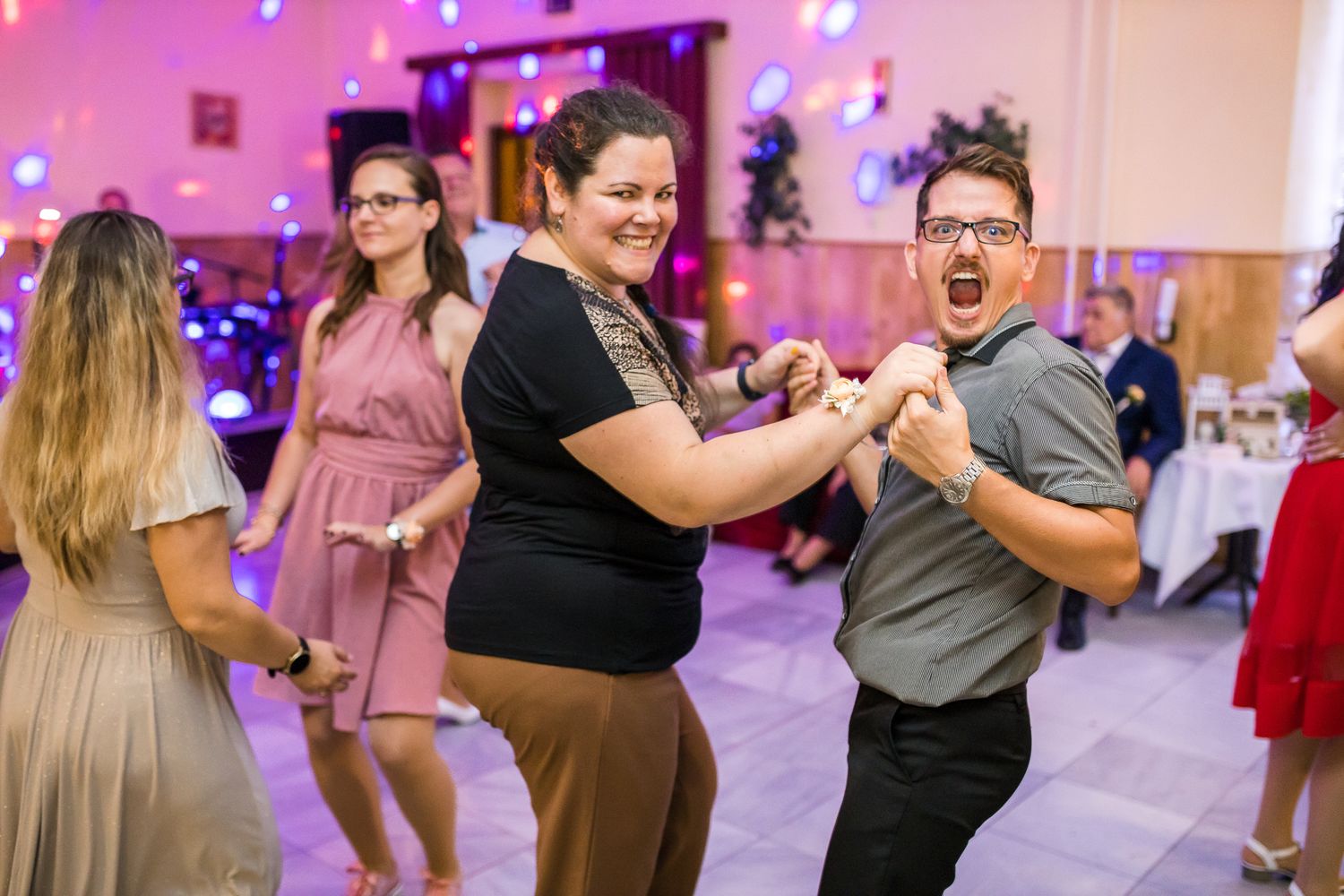 People dancing and having fun at a party with pink lighting and festive decorations in the background.