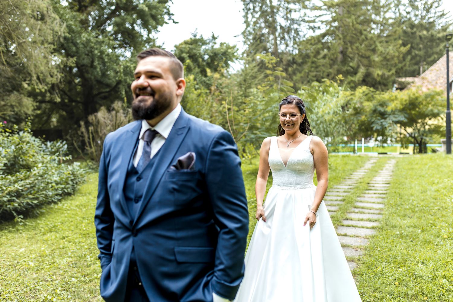 A wedding couple shares a joyful moment together in a lush garden setting with stone pathways.
