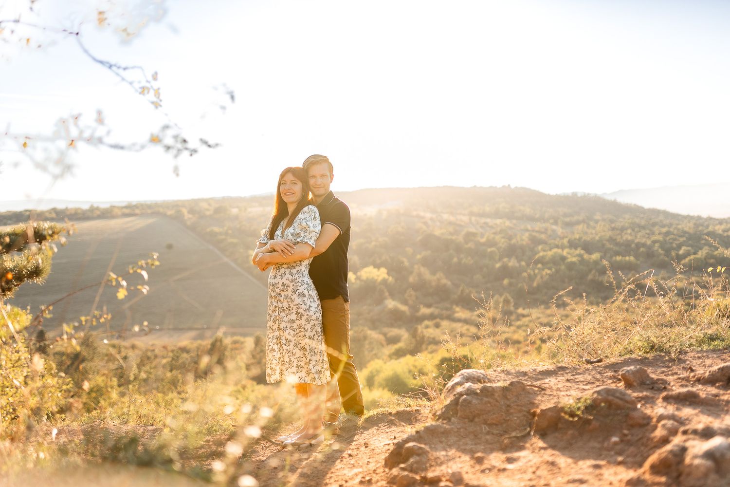 Silhouettes of couple against golden sunset landscape on rocky terrain.