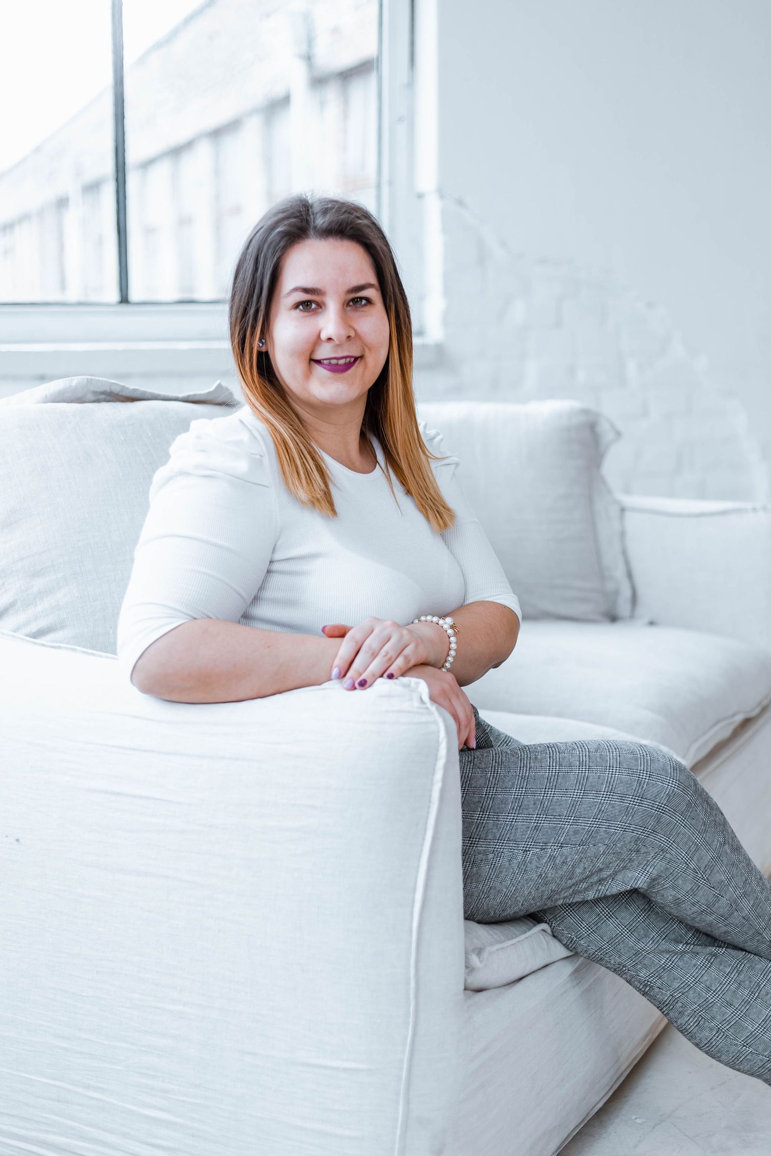 Woman lounges comfortably on white sofa in modern bright interior.