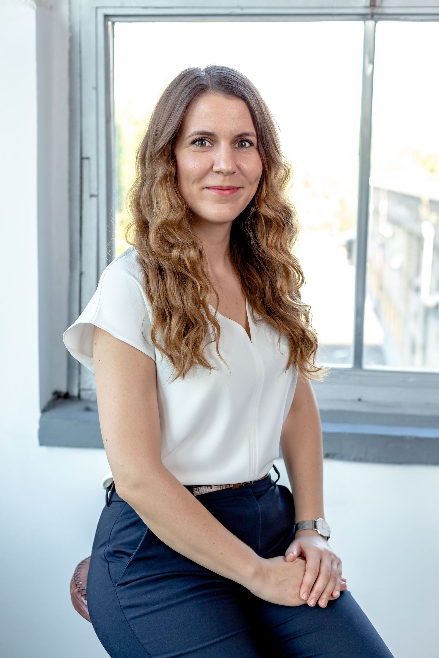 Professional headshots in bright studio with white top and dark pants near window.