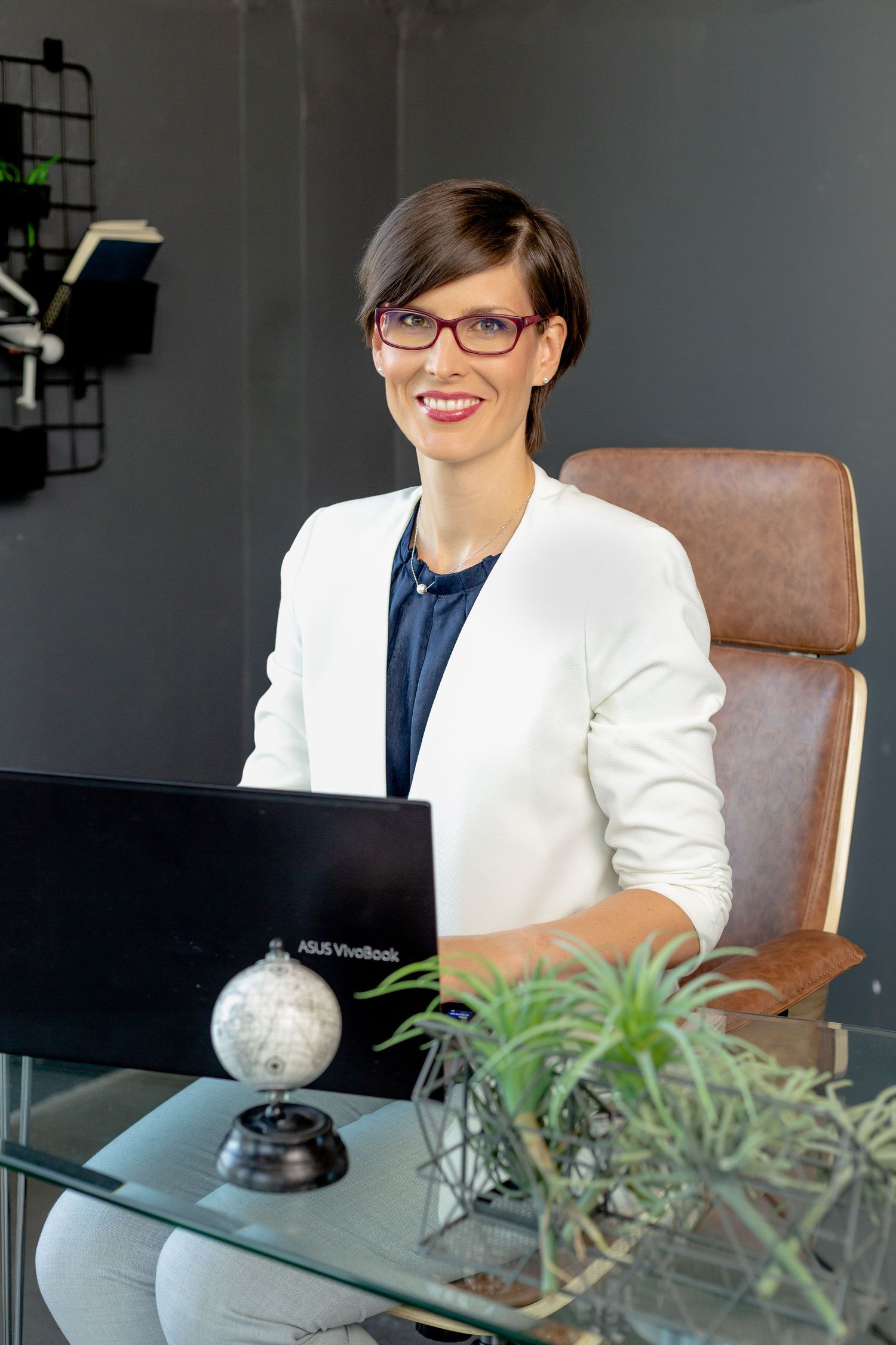 Modern office setting with leather chair, plants and laptop showing professional workspace design.