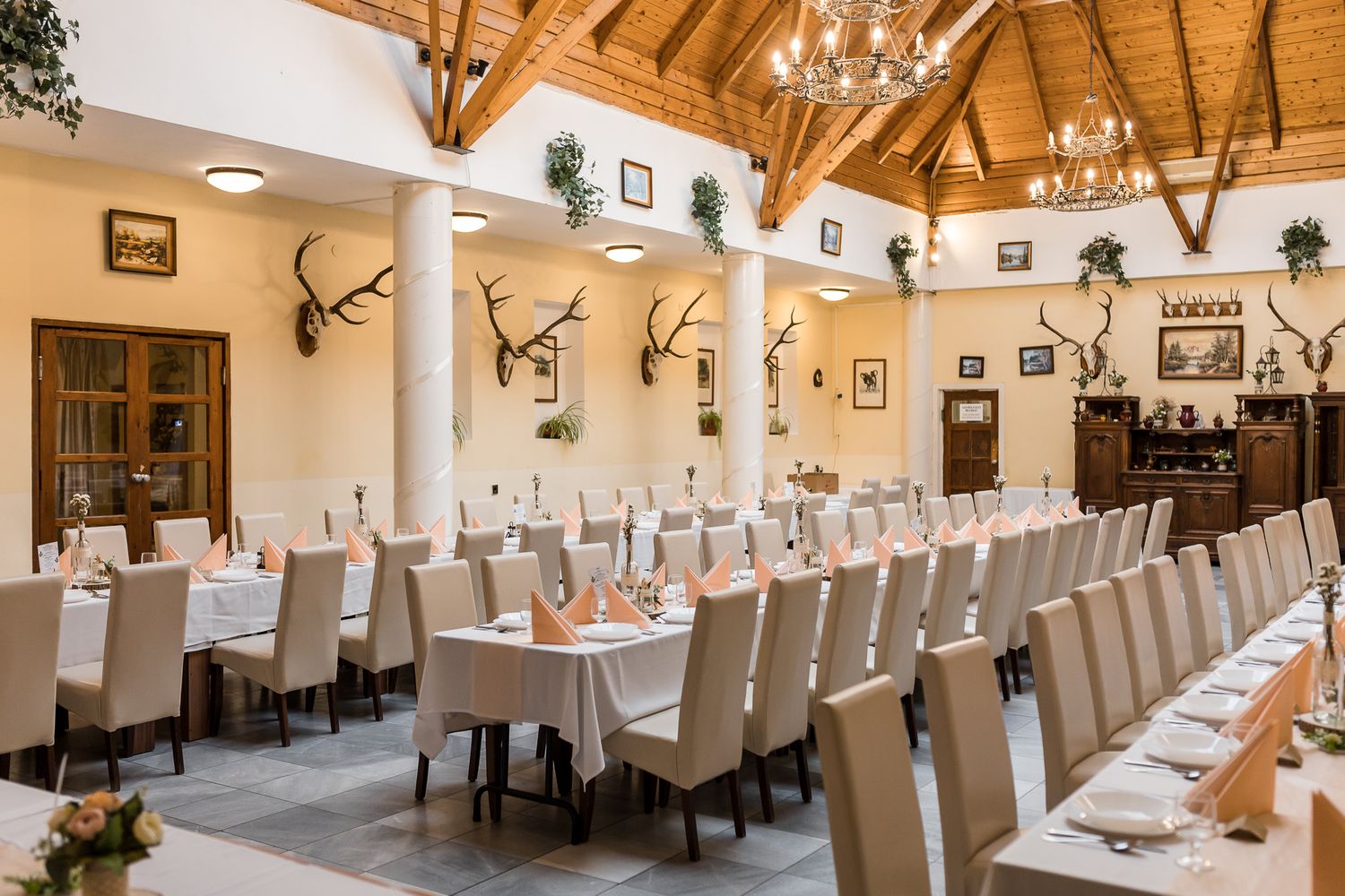 Long banquet hall setup with white-covered chairs and wooden beam ceiling for an elegant wedding reception.