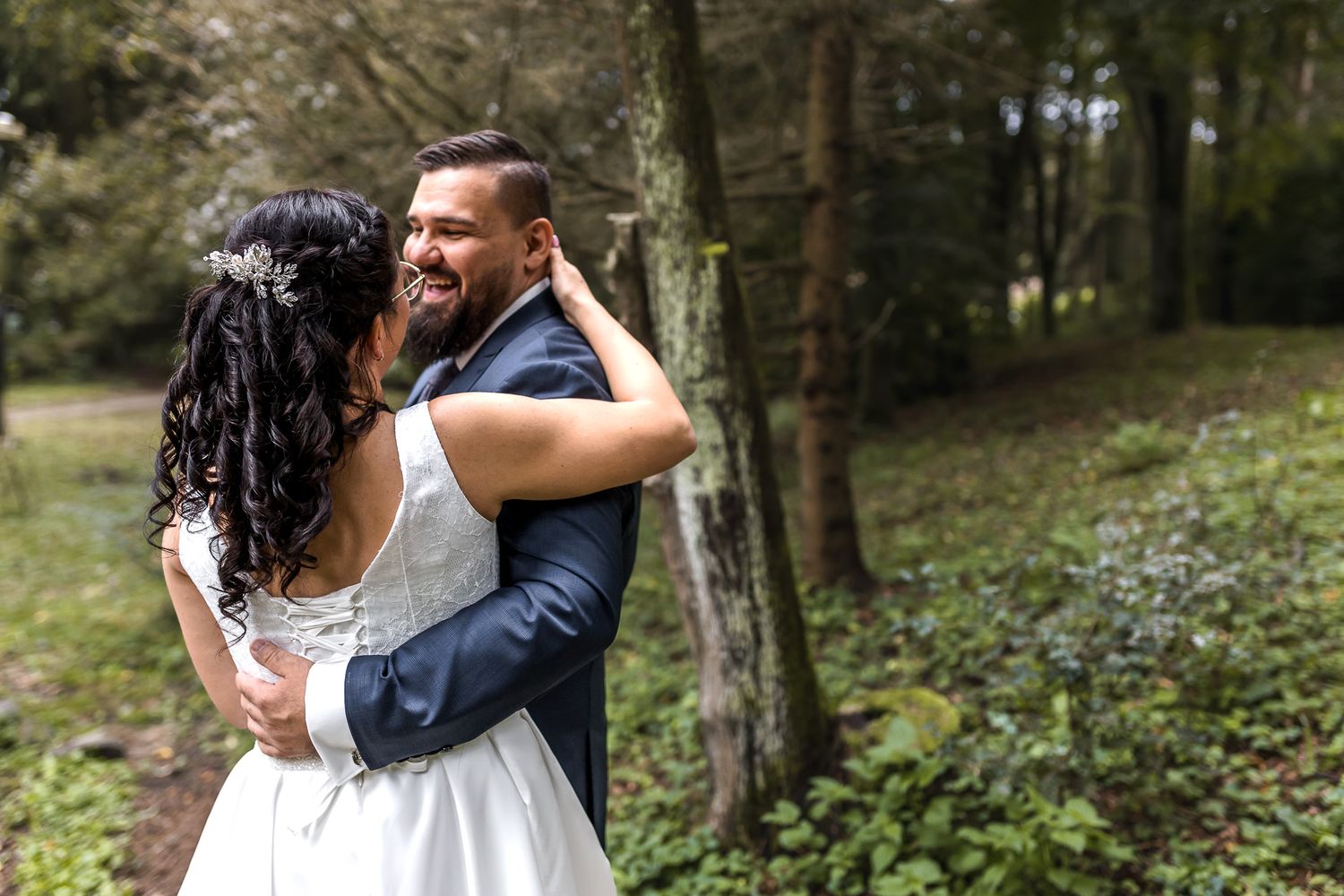 A couple in formal attire embraces while dancing in a lush forest setting during a romantic outdoor celebration.