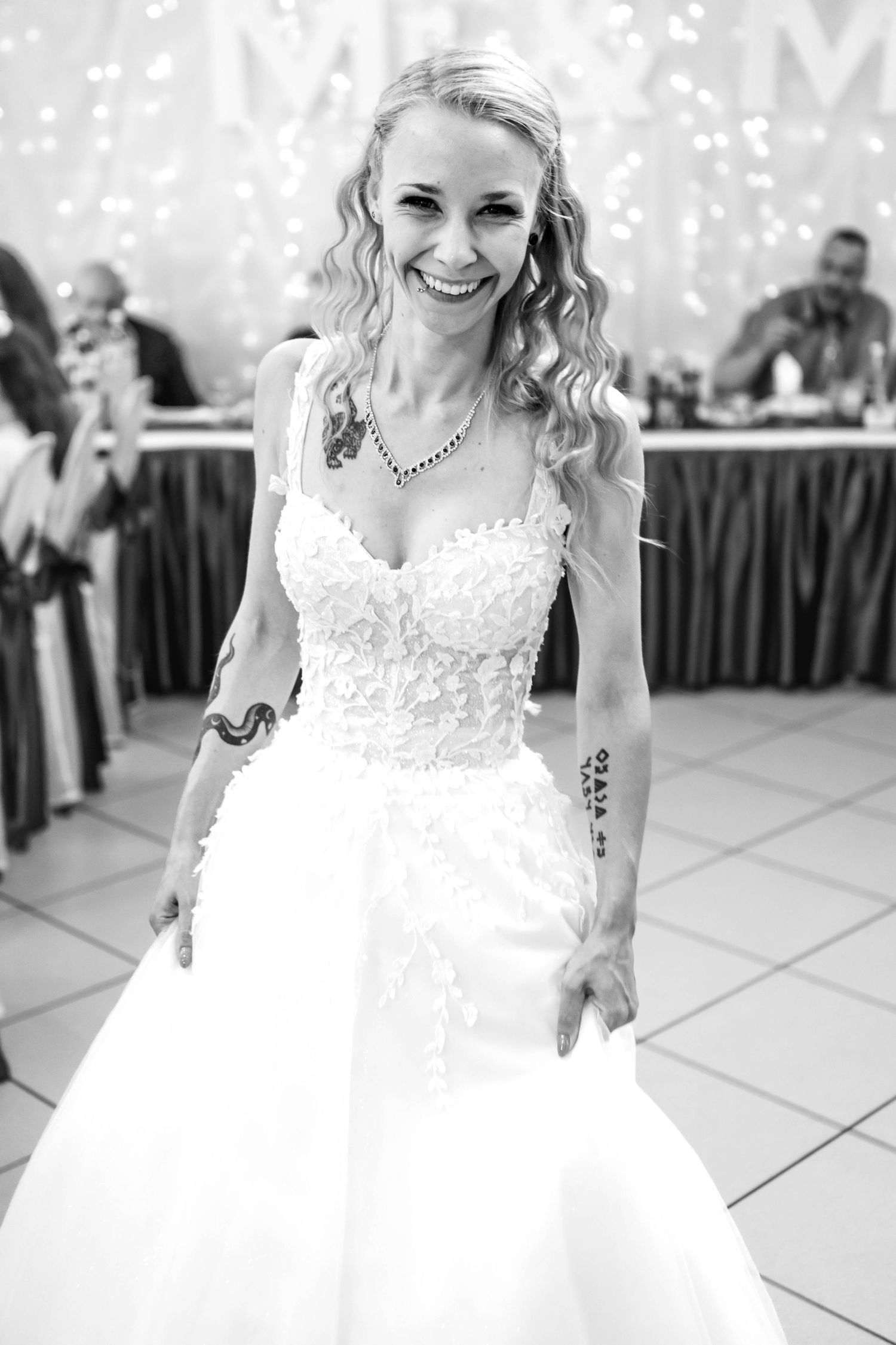 A series of black and white wedding photos showing a bride in a white lace dress dancing and smiling at a reception.