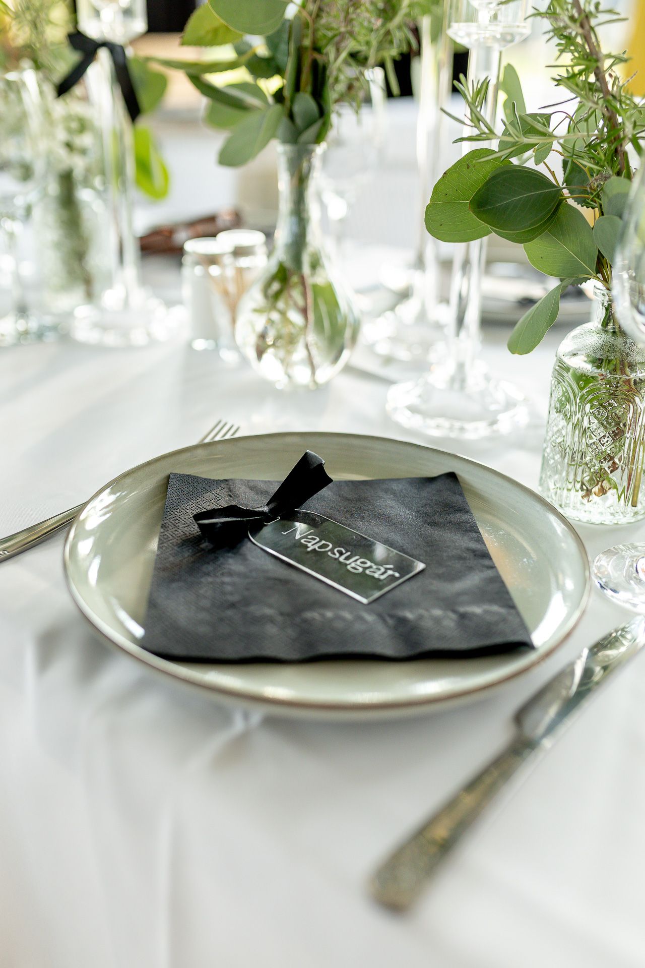 Wedding reception table settings with fresh greenery and black napkin accents.