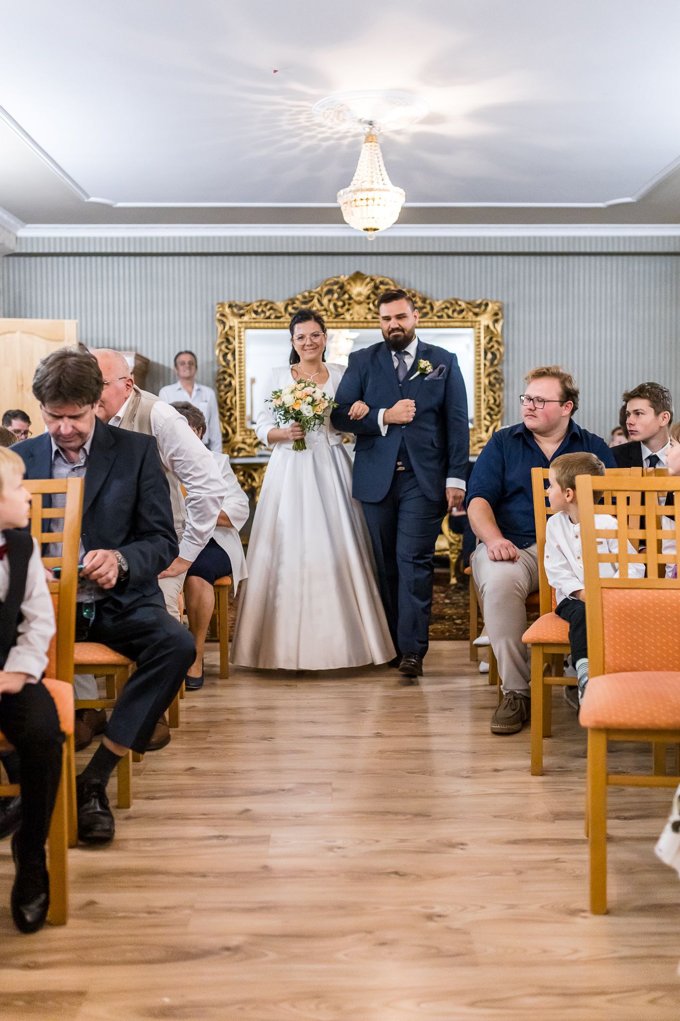 A series of wedding guests perform the traditional shoe game at a reception on a wooden dance floor.