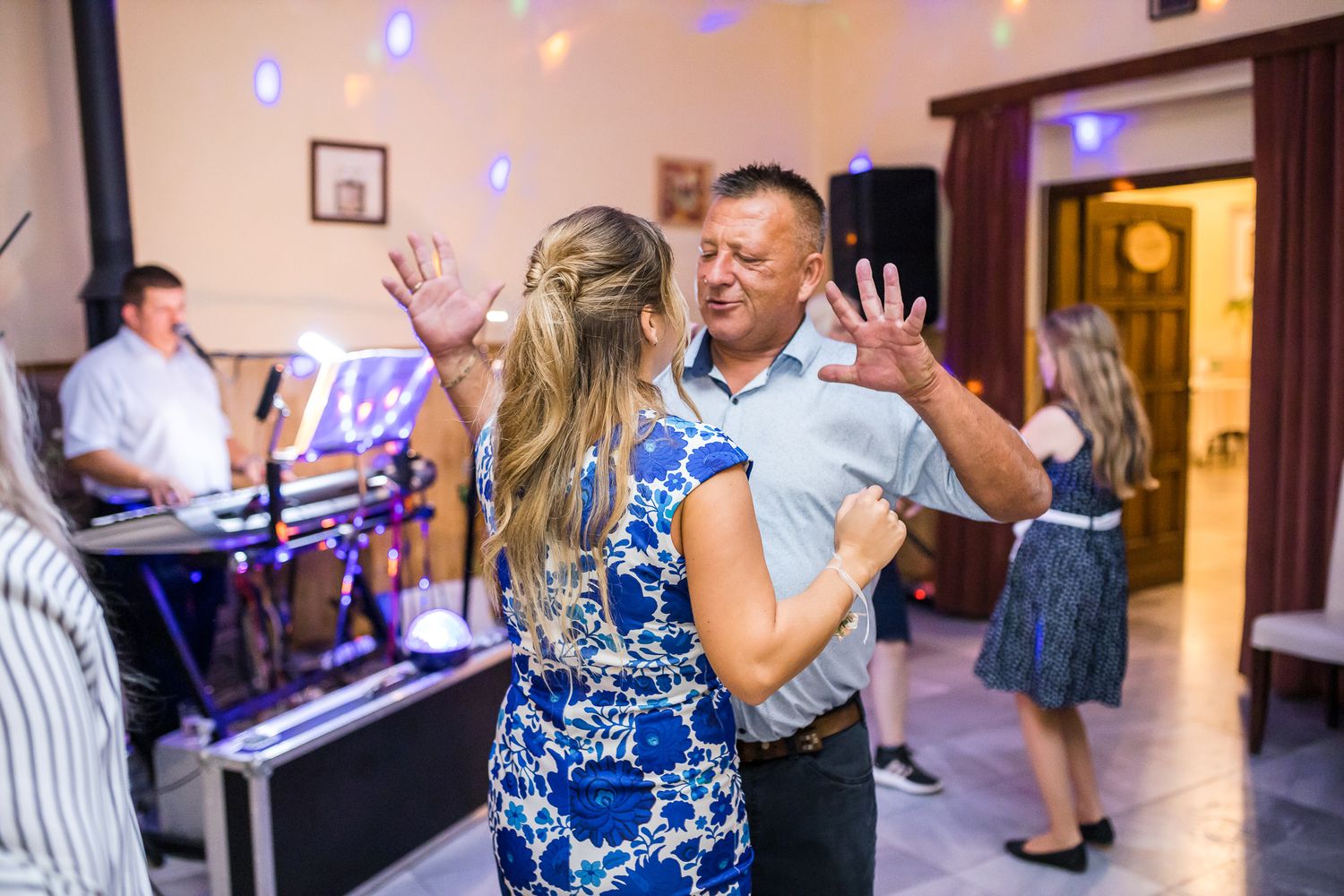 People dancing and celebrating at a wedding reception with blue lighting and wooden decor in an indoor venue.